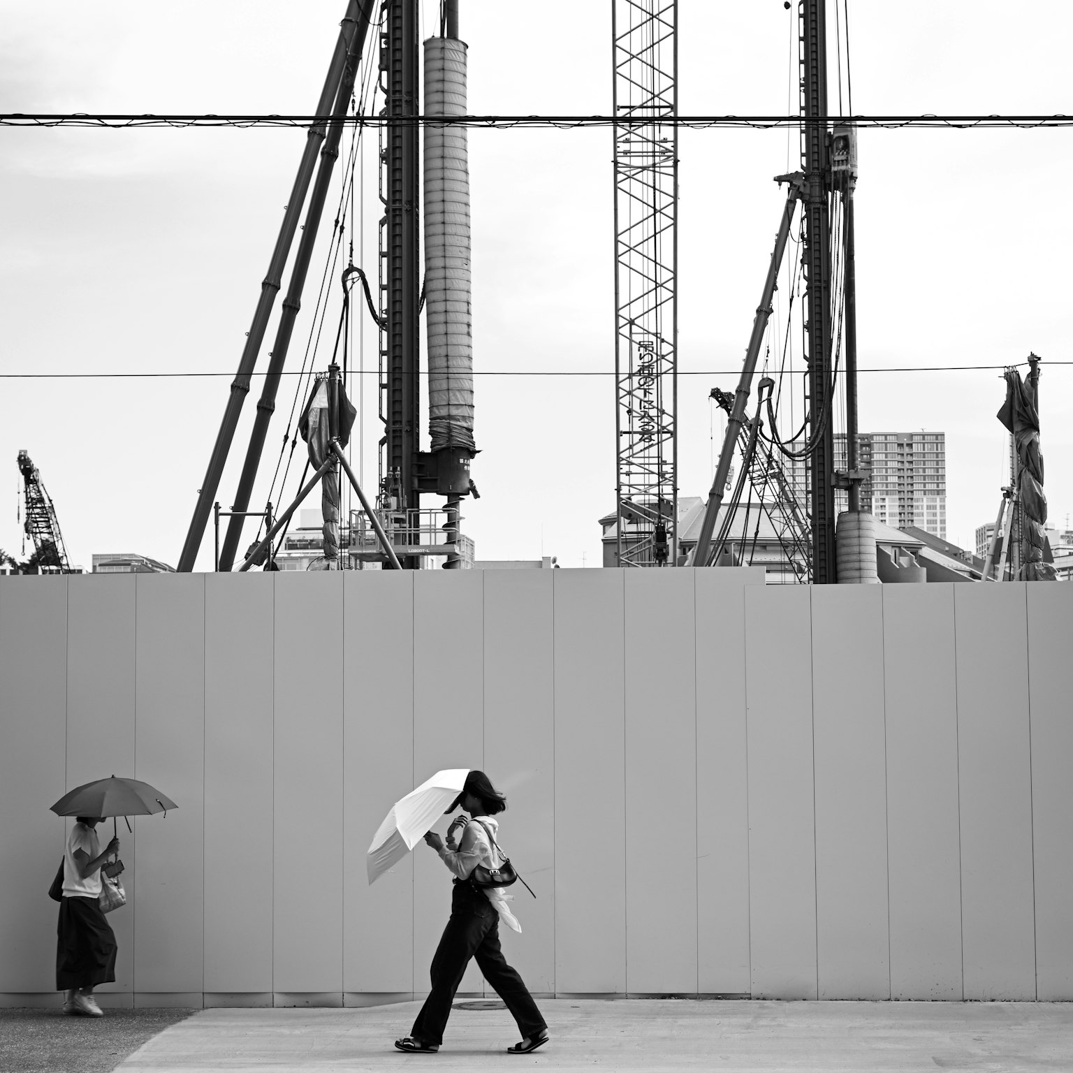 Schwarzweißfoto von Menschen, die vor einer Baustelle mit Regenschirmen gehen