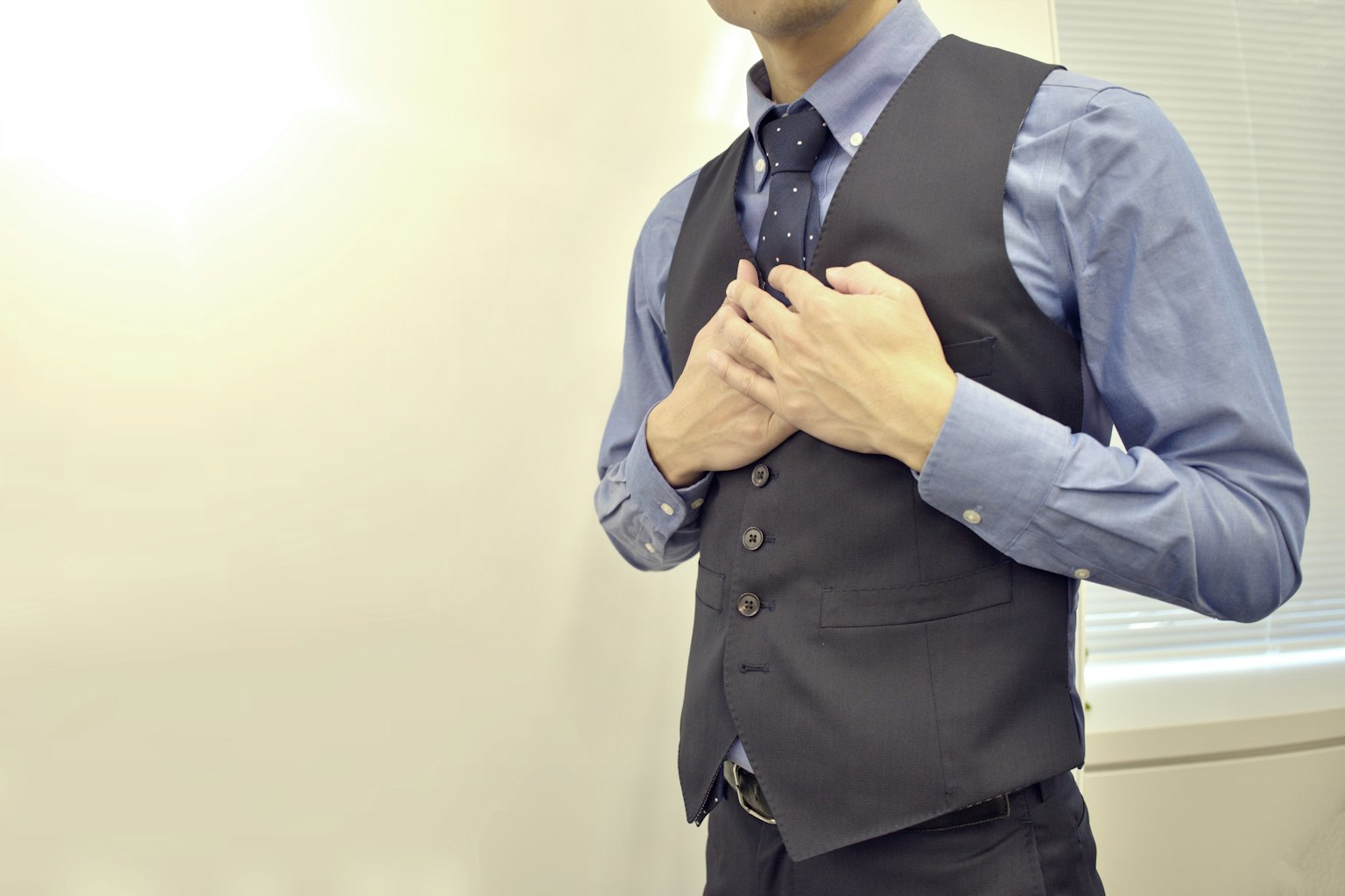 Man adjusting his vest while wearing a blue shirt and tie