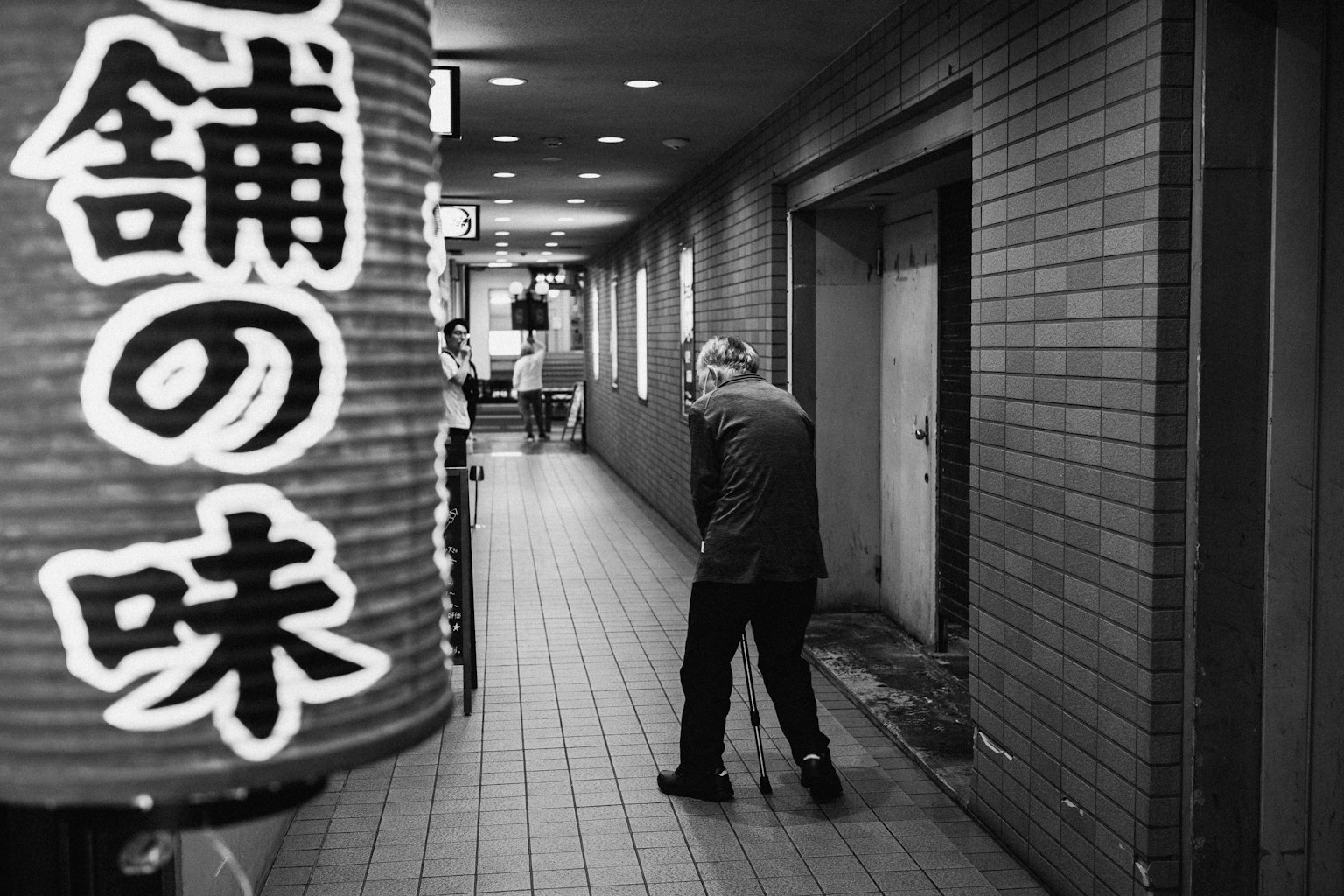 Elderly man walking in a narrow corridor with a red lantern sign