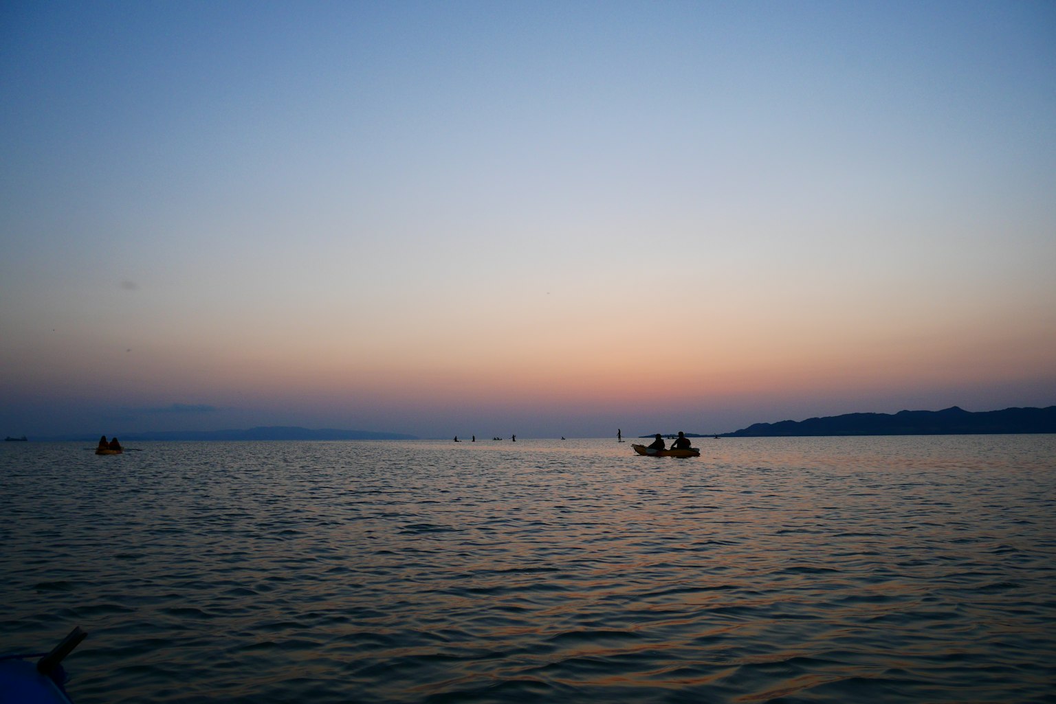 Calm water surface with sunset sky over the sea several small boats visible