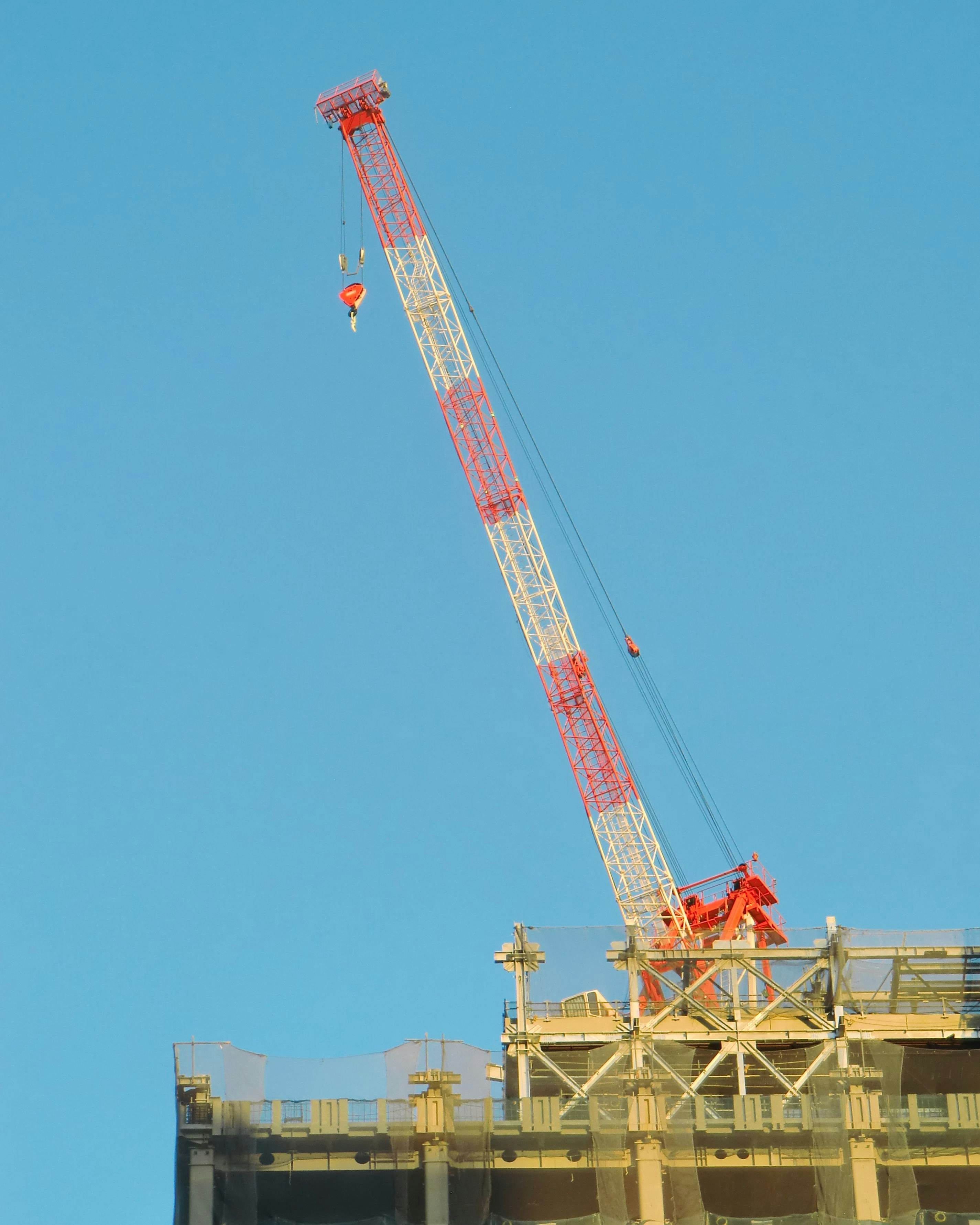 青空に伸びるクレーンと吊り荷のある建設現場の一角