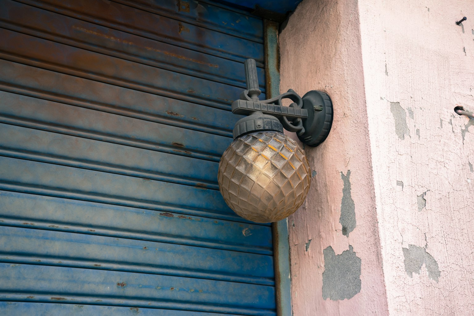 Un luminaire vintage avec un abat-jour doré à côté d'un volet bleu et d'un mur usé