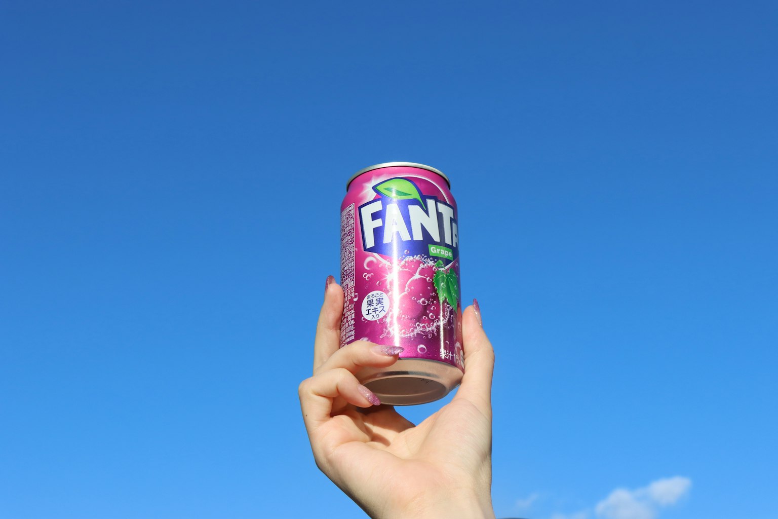 Hand hält eine Fanta-Dose vor einem klaren blauen Himmel