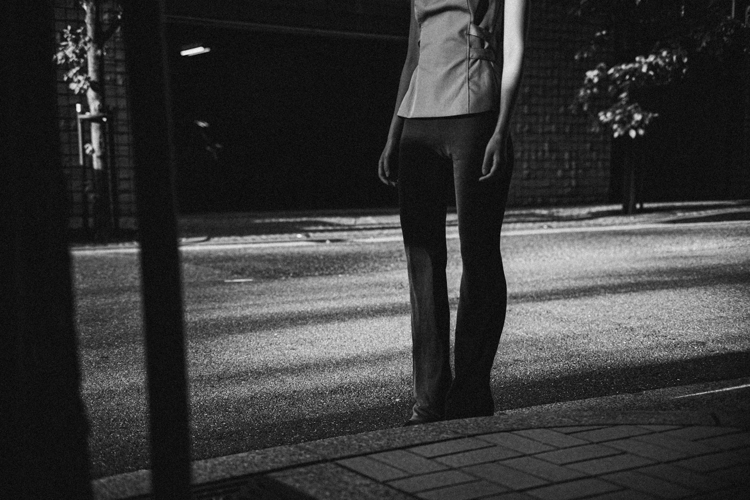 モノクロの街角で立つ女性の全身像 街灯の影が印象的