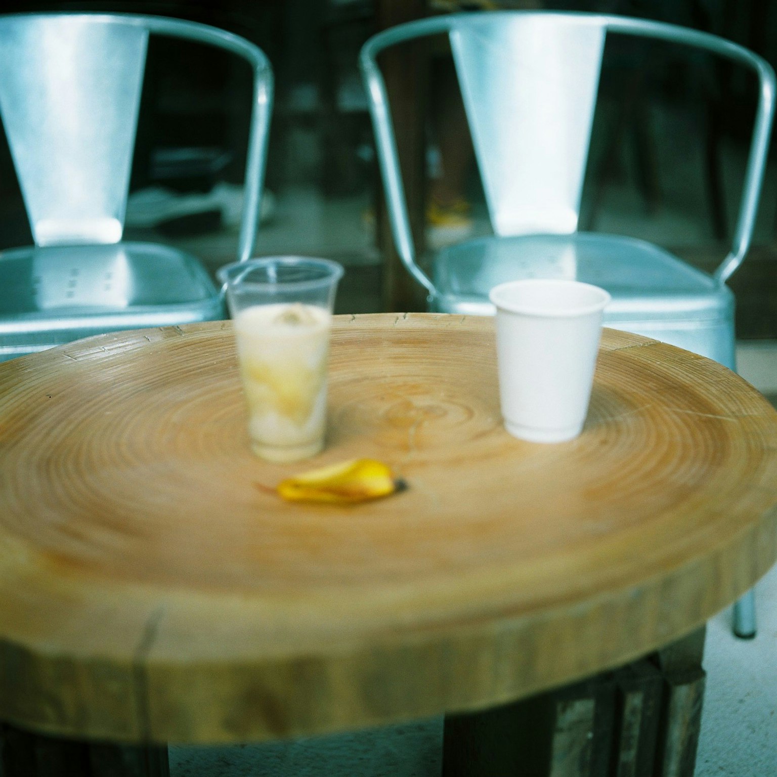 Una mesa de madera con bebidas y un plátano encima un vaso transparente y un vaso blanco están colocados uno al lado del otro