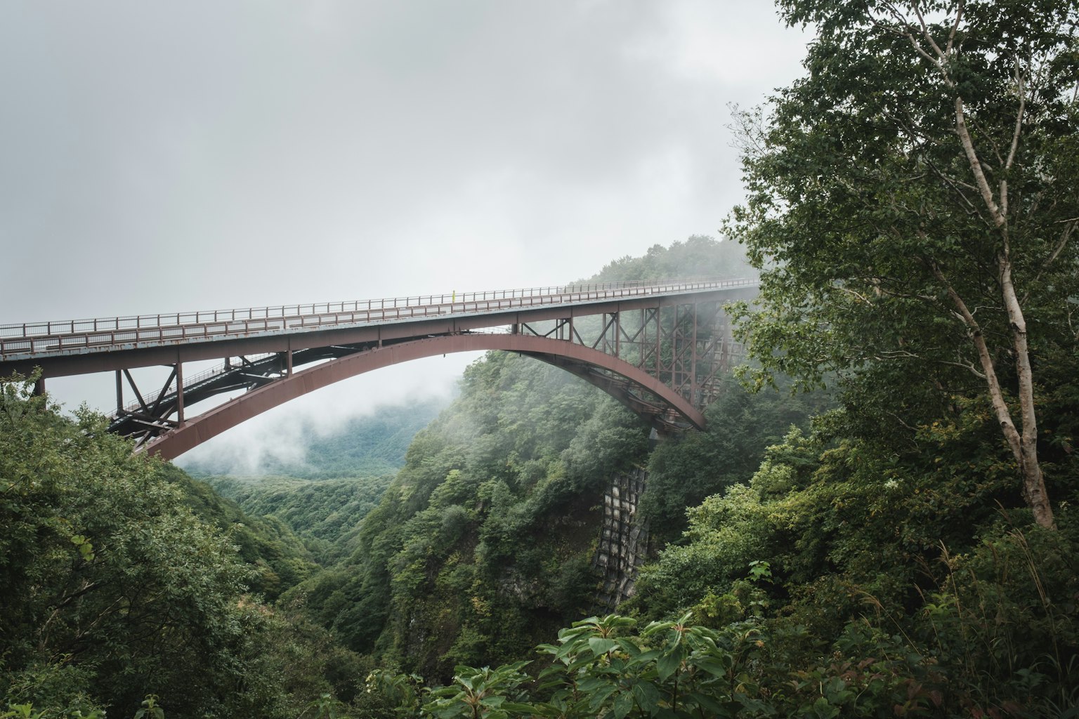 Red arch bridge surrounded by lush green mountains in fog