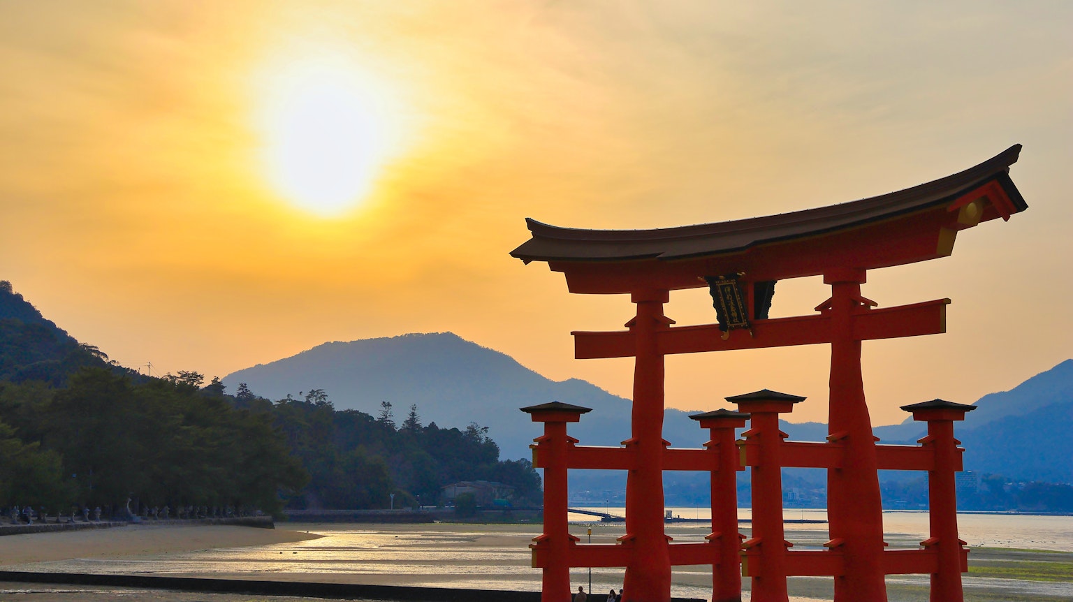 Red torii gate silhouette against a sunset with mountains