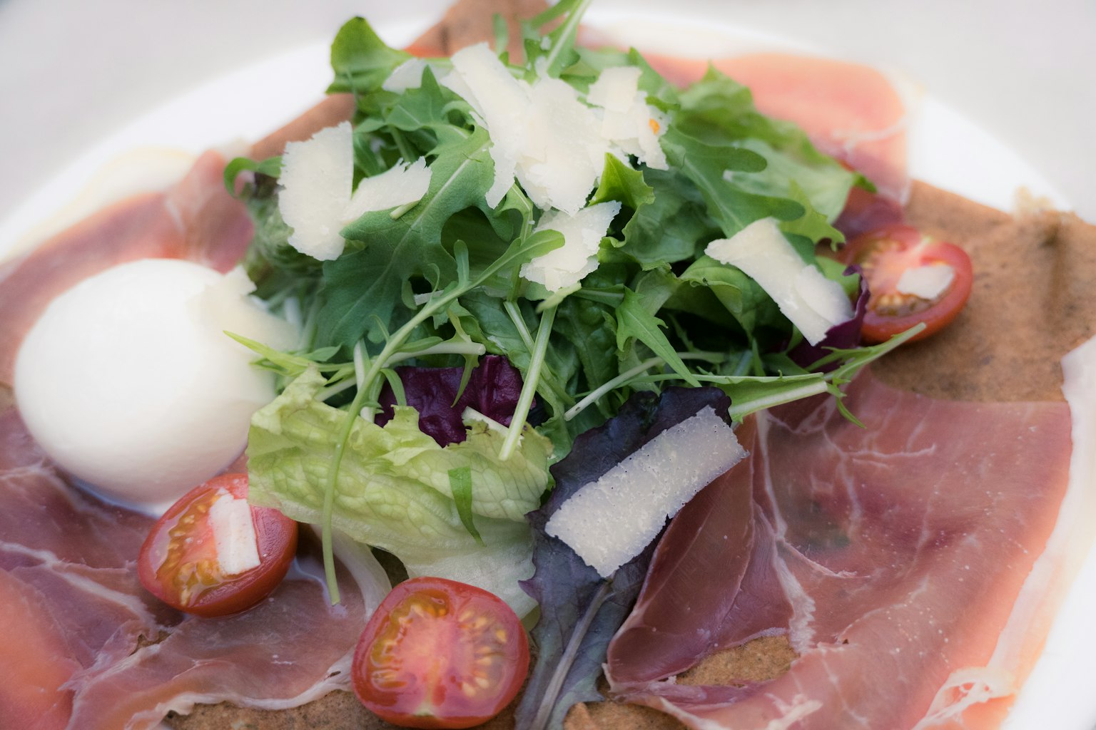 Hidangan dengan prosciutto dan salad yang dihiasi telur poached