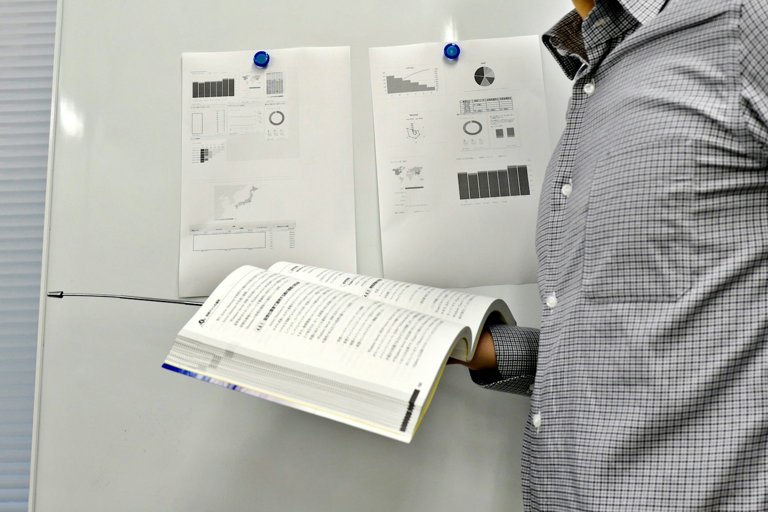 Un uomo in camicia a quadri tiene un libro davanti a una lavagna con grafici appesi