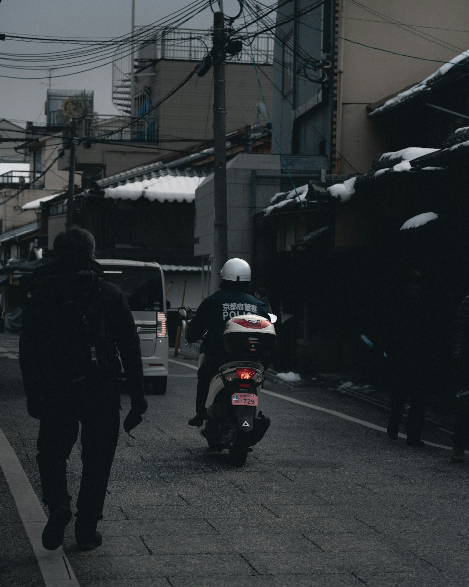 在雪天的城市街道上行走的人和送貨摩托車