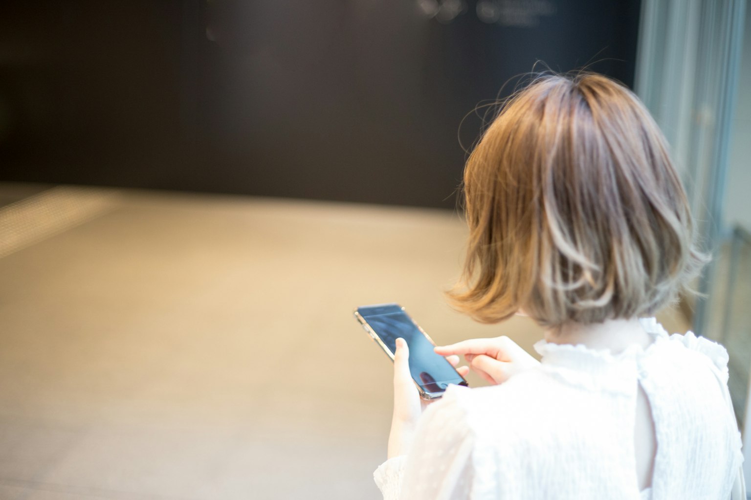 Foto di una donna che tiene uno smartphone di spalle con capelli corti e abbigliamento chiaro