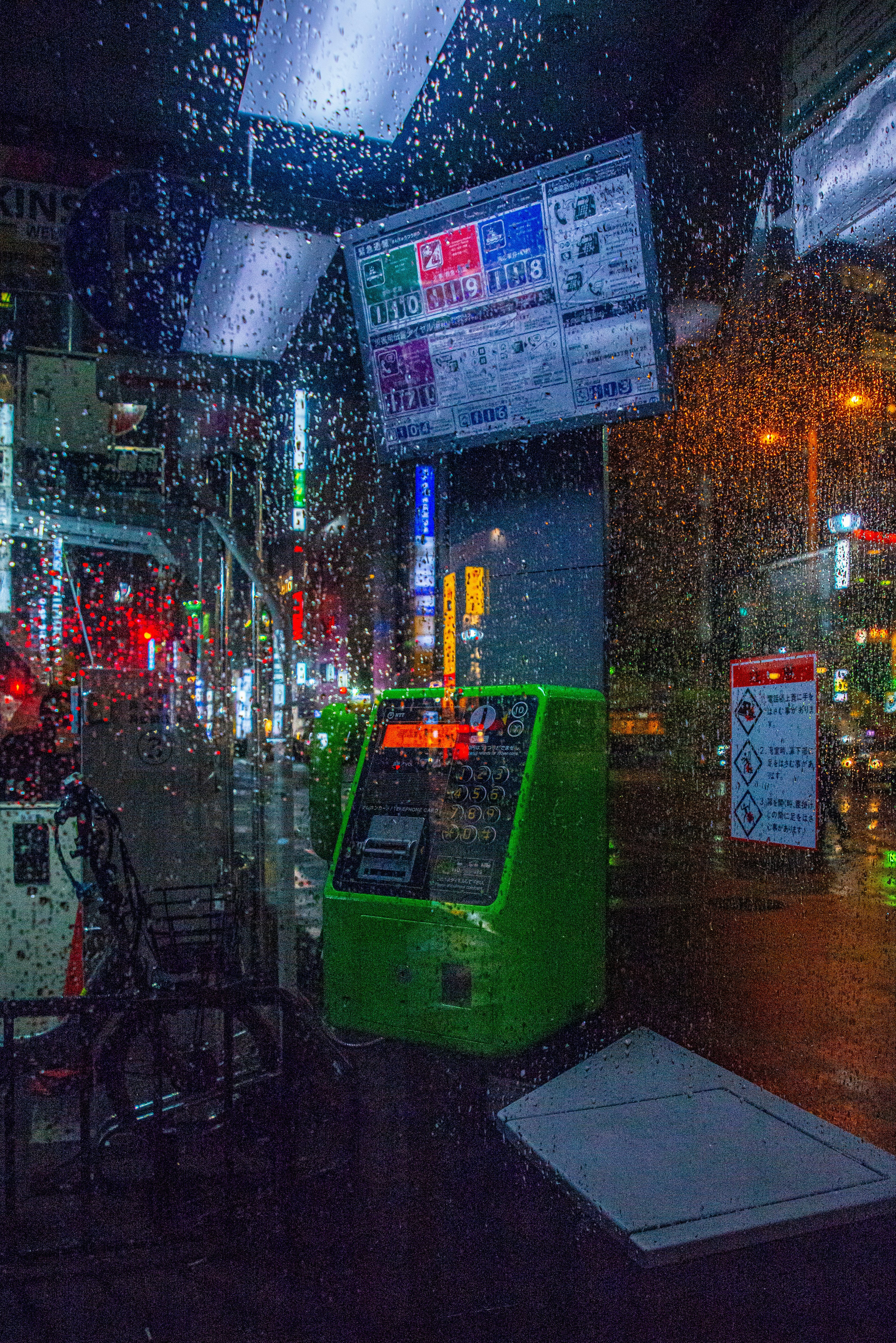 雨の夜にネオンがにじむ街角の掲示板と自販機