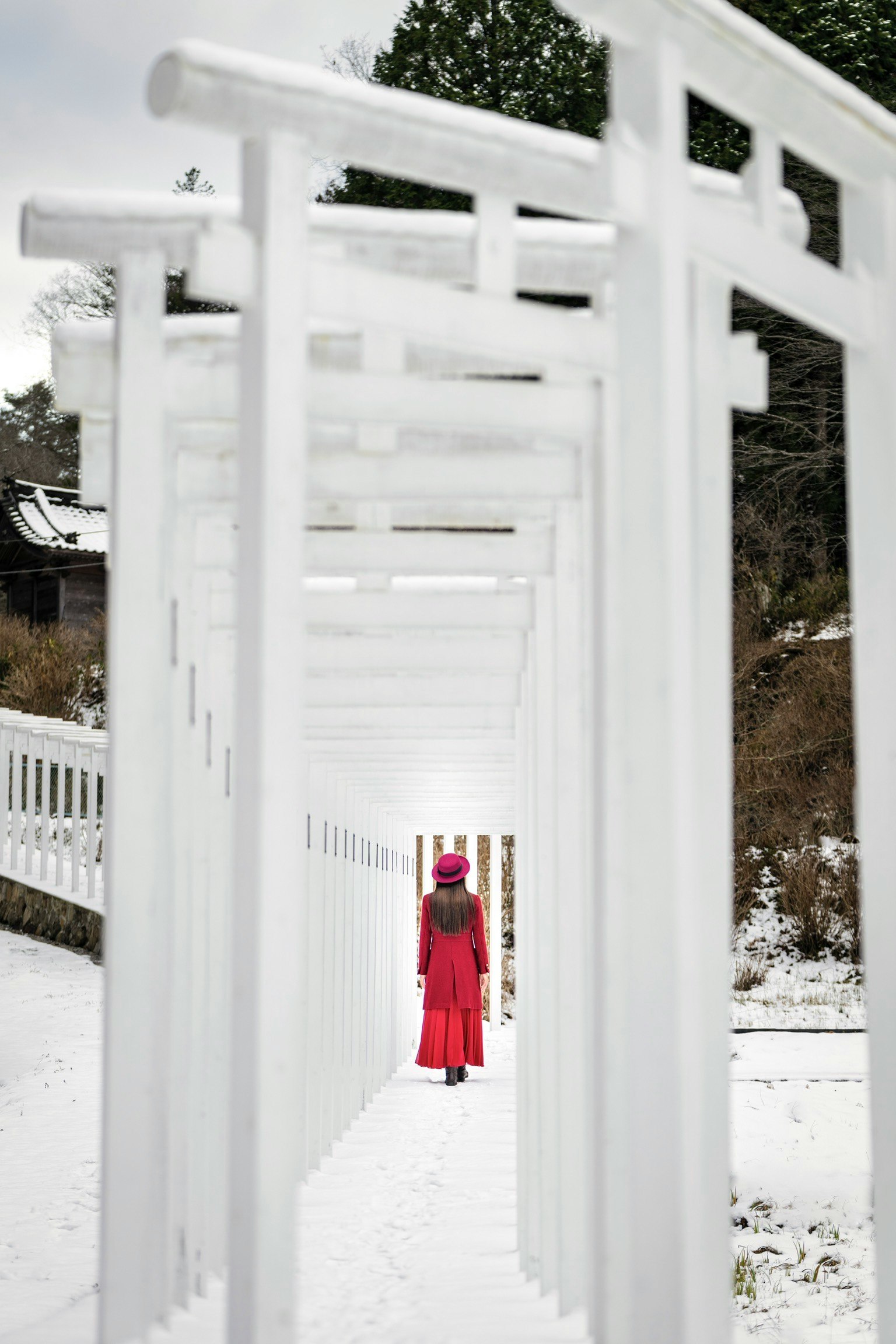 Frau im roten Kimono, die durch die verschneiten Senjō-Torii von Saido-ji geht