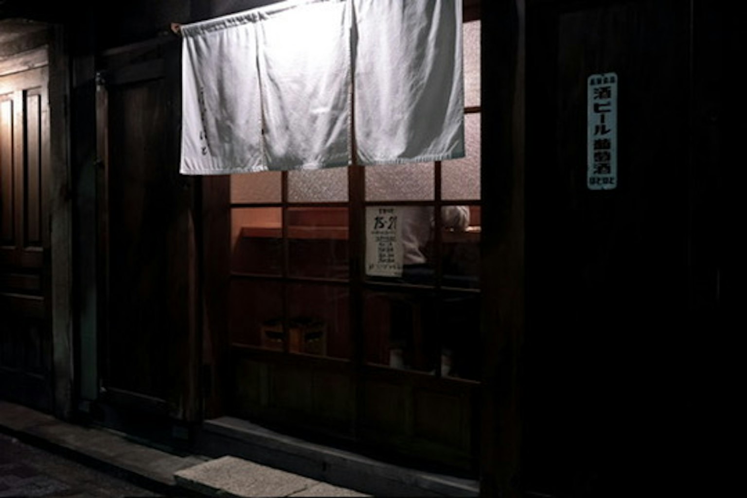 Exterior of a traditional Japanese izakaya on a dark street with a white noren hanging