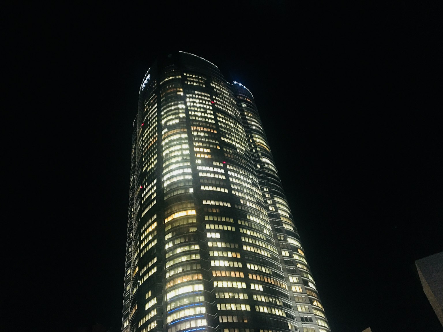 Imagen de un rascacielos iluminado por la noche con un fondo oscuro