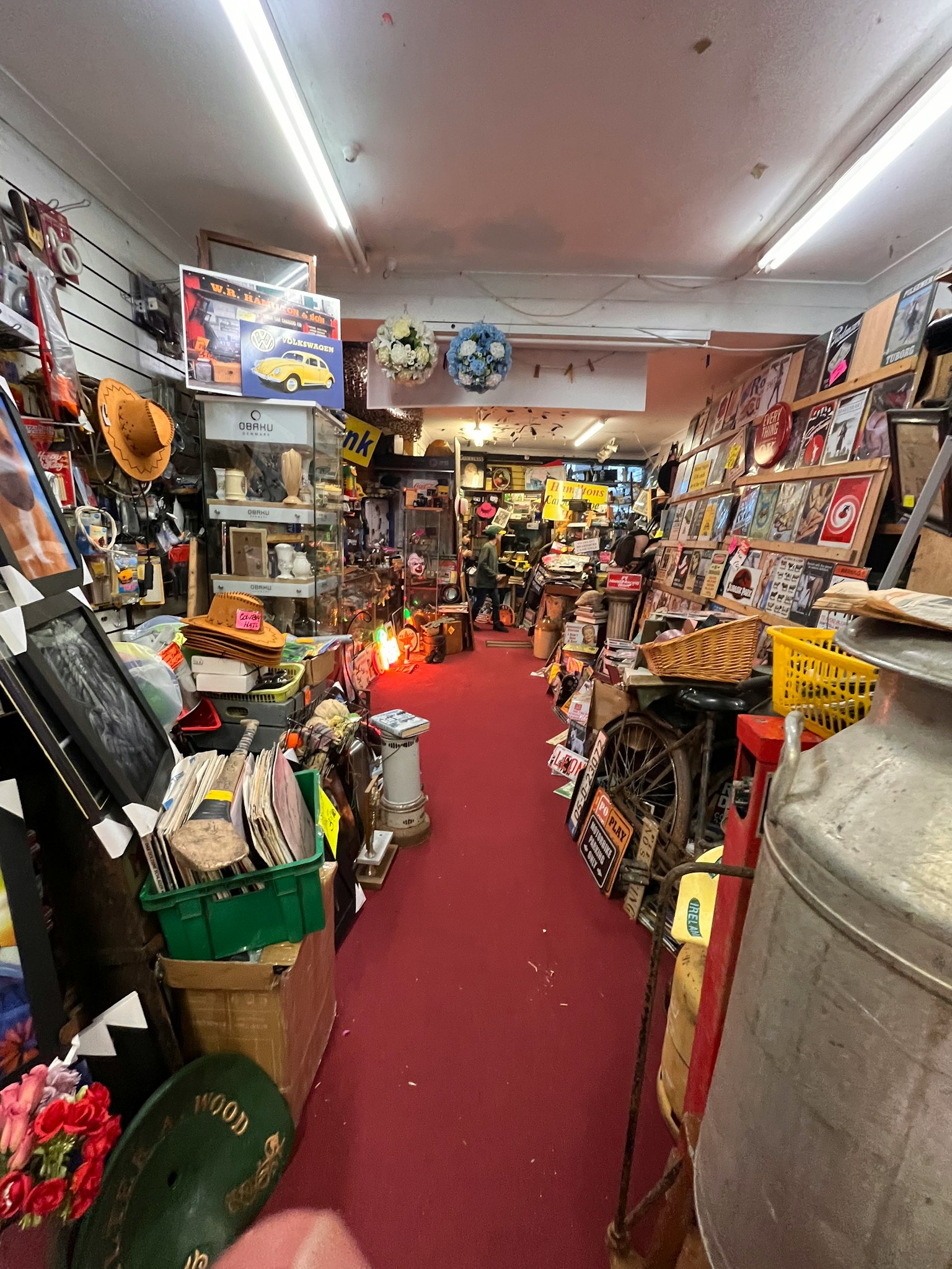 拥挤的古董店内狭窄过道两侧摆满书籍和收藏品地面有红色地毯