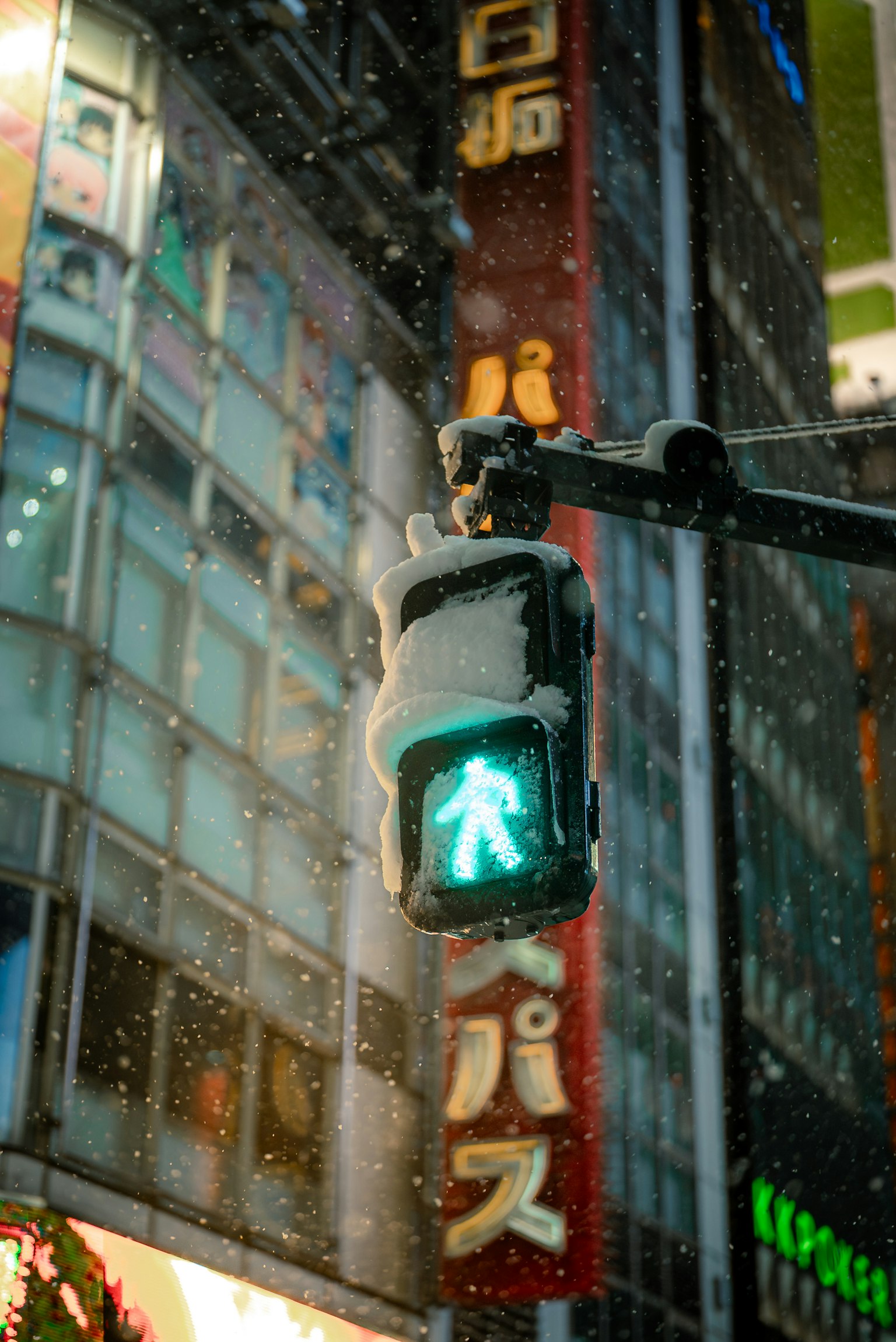 Signal piéton vert illuminé sous la neige avec des enseignes au néon en arrière-plan