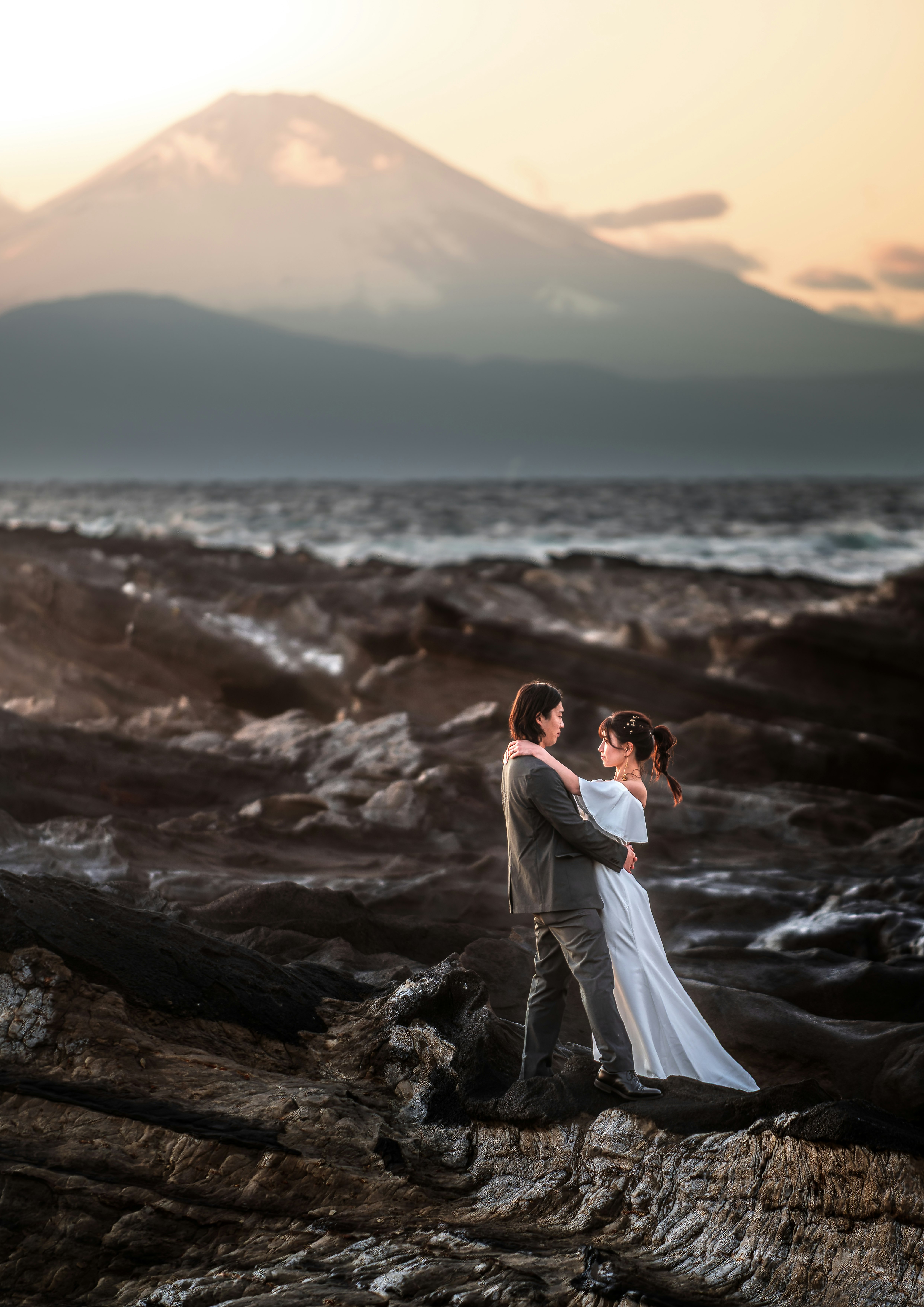 溶岩の岩場に立つウェディングカップルと富士山の夕景