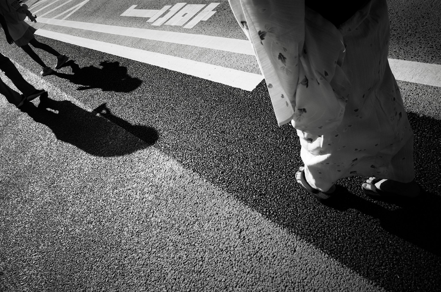 Schatten und Kleidung von Personen, die auf einer Schwarz-Weiß-Straße gehen