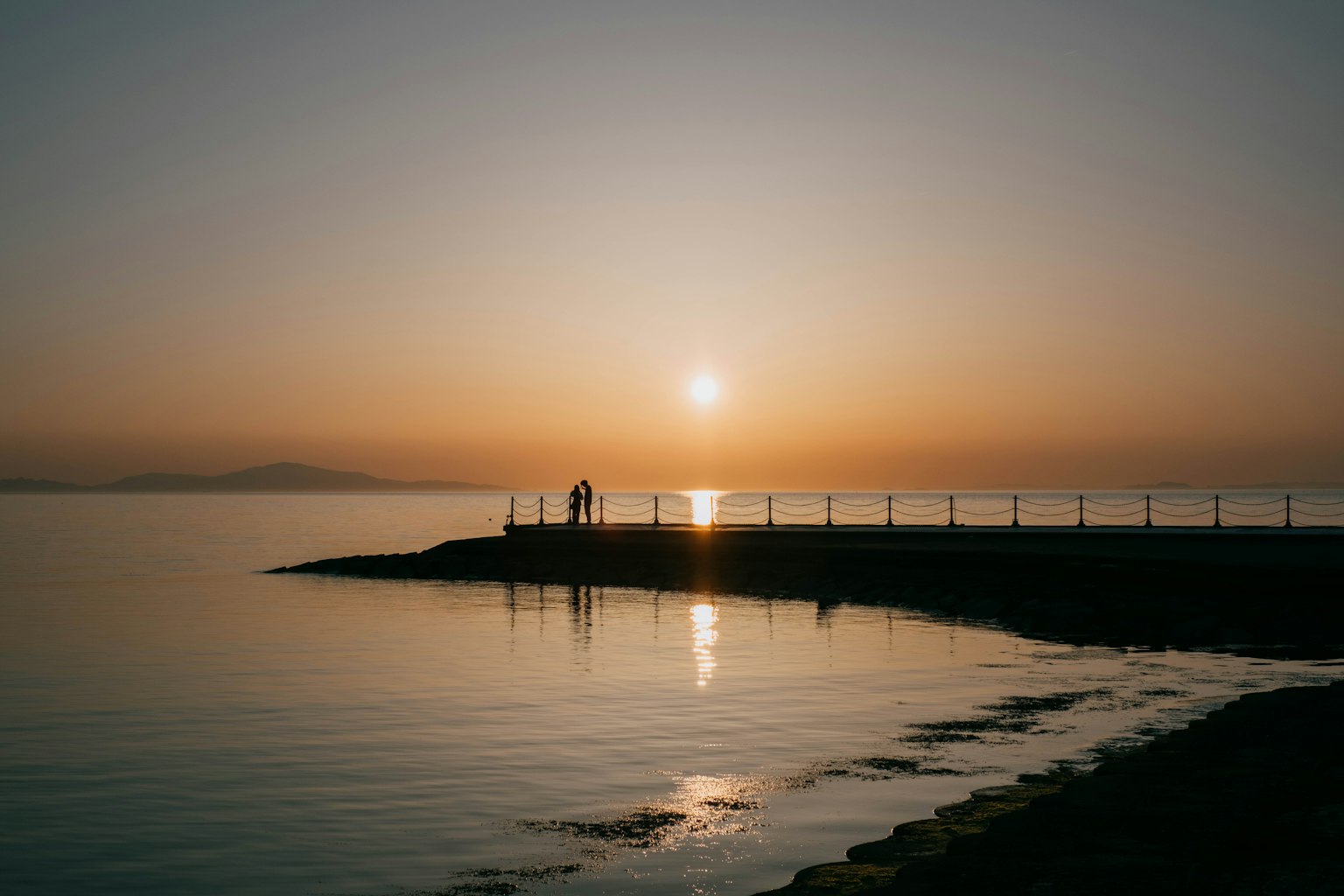 Puesta de sol sobre aguas tranquilas siluetas de personas en la orilla