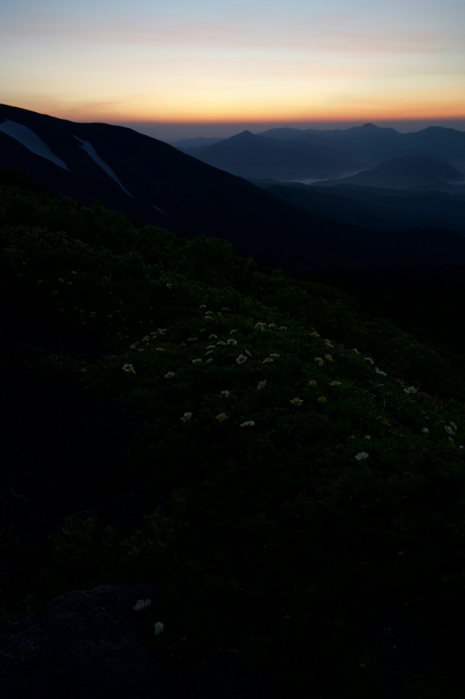Pemandangan pegunungan saat senja dengan rumput hijau dan gunung jauh