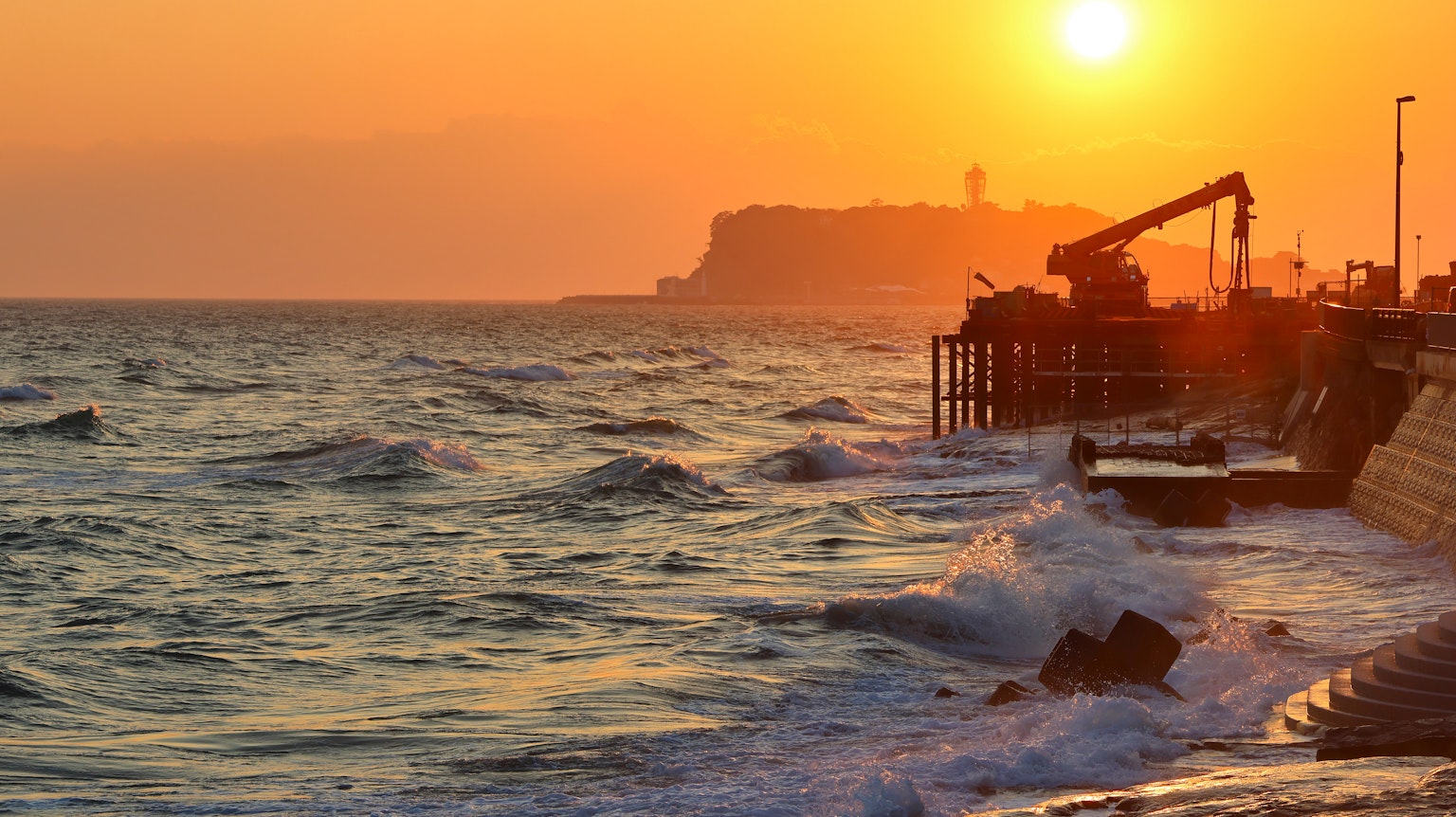 Matahari terbenam di atas lautan dengan ombak menghantam pantai
