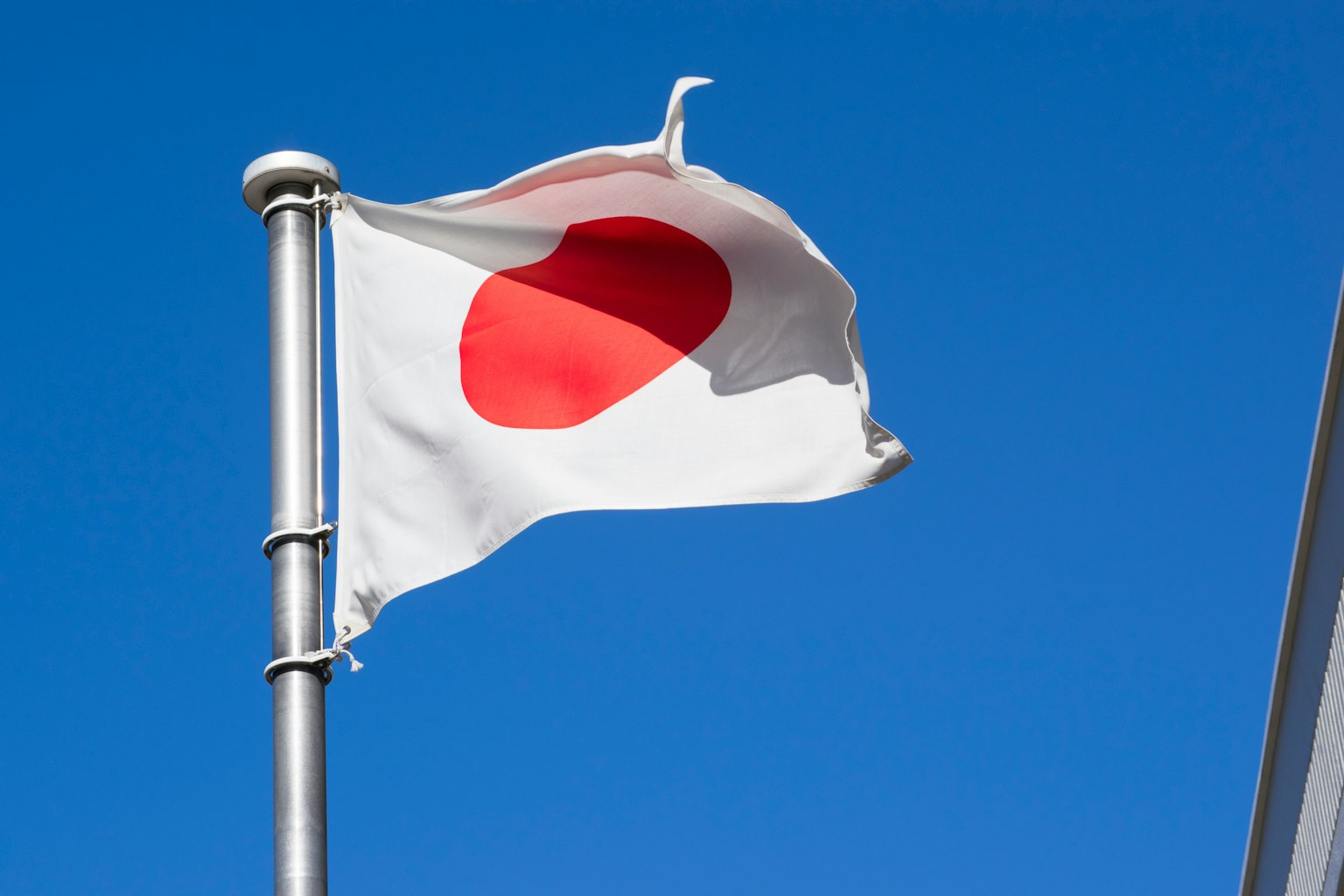 Japanese flag waving under a blue sky featuring a white background with a red circle