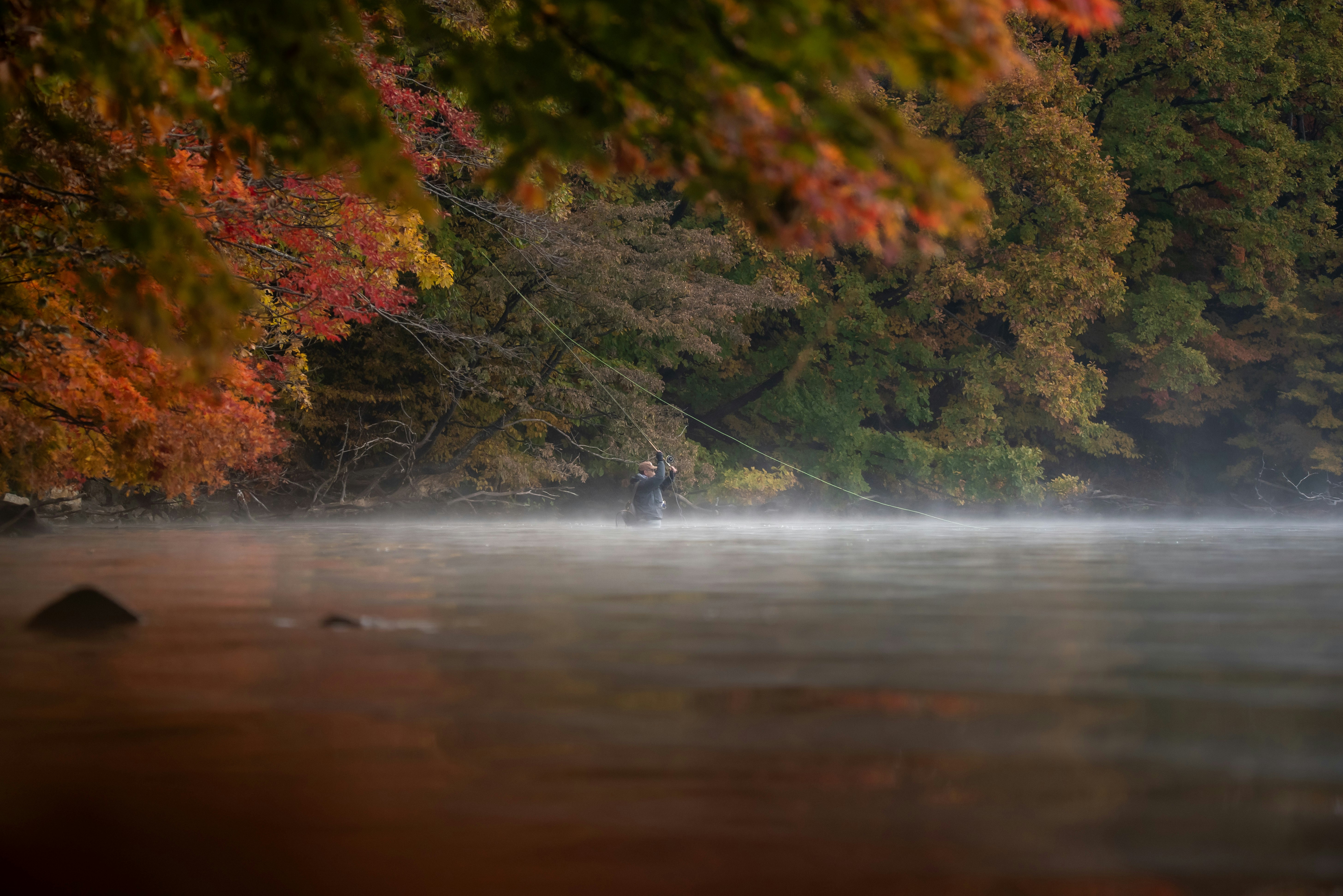 Pêcheur au bord d’une rivière entourée de feuillage d’automne, matin brumeux