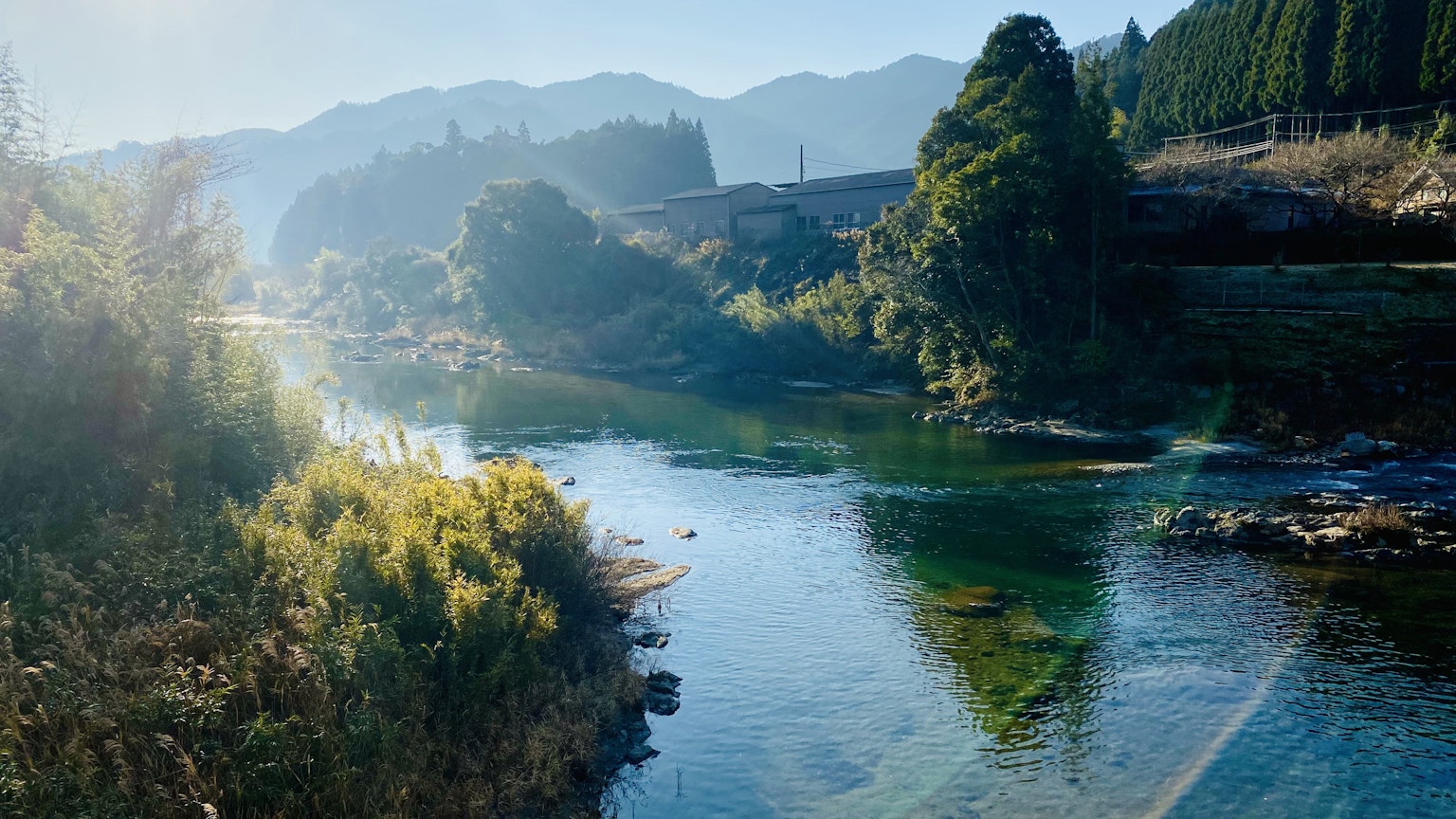 Paisaje de río sereno con montañas, agua azul y vegetación exuberante