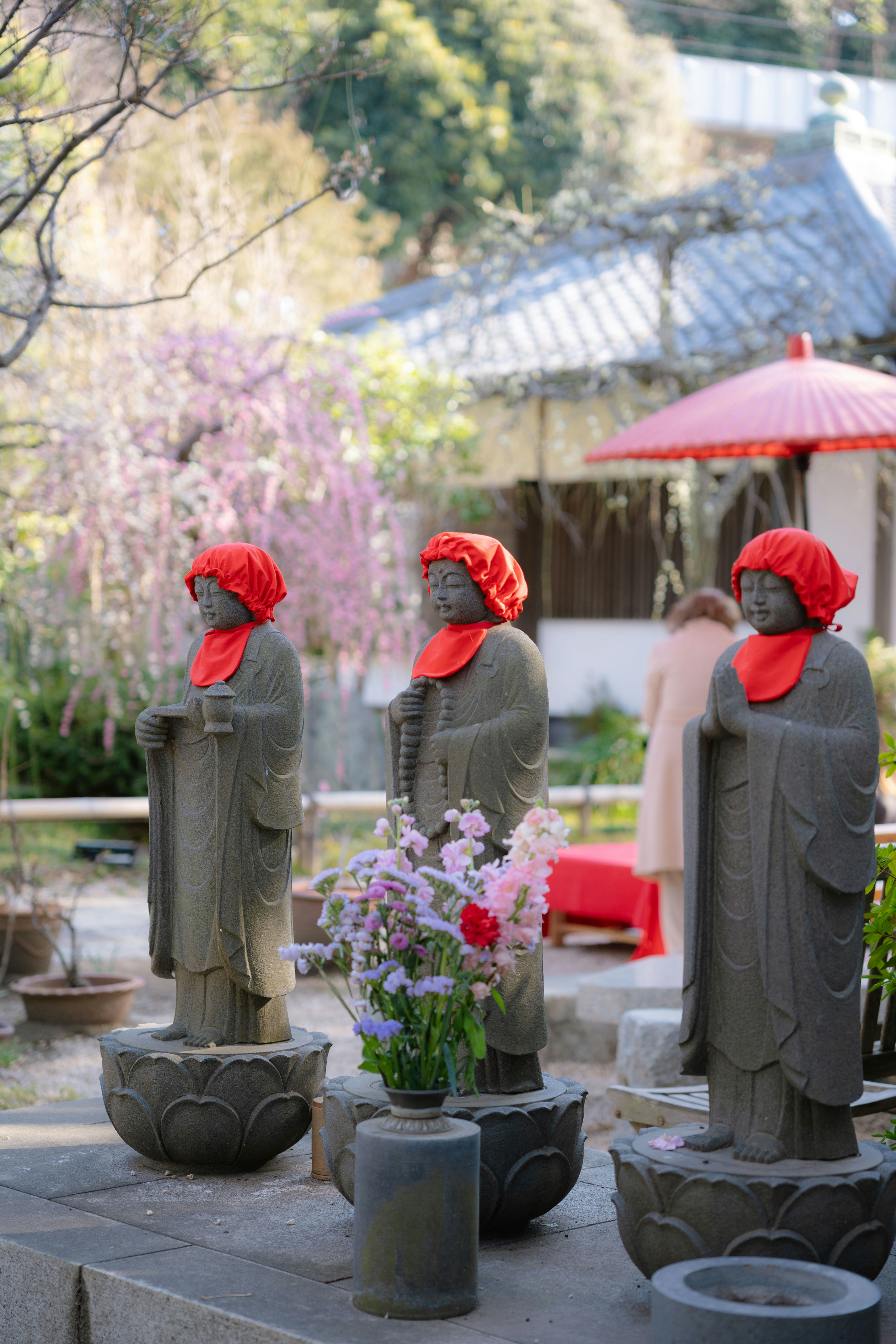 赤い帽子を被ったお地蔵様と花の並ぶ寺の境内