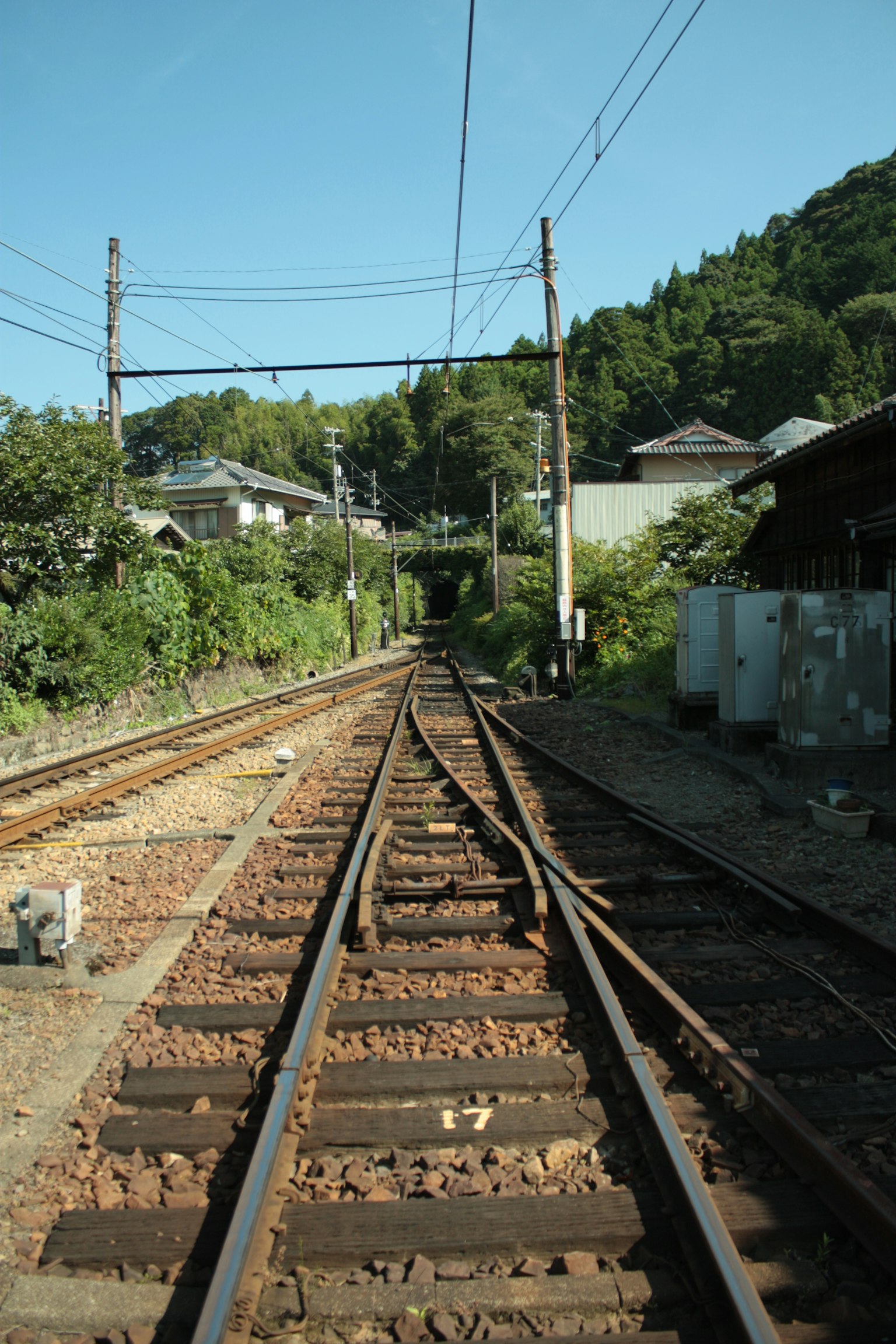 ทัศนียภาพของรางรถไฟที่ยาวไปในระยะไกล เนินเขาสีเขียวอยู่ในพื้นหลัง บ้านที่มองเห็นได้