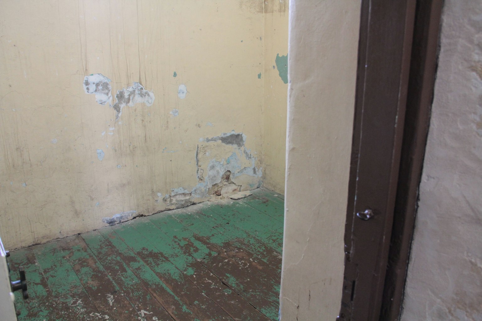 Interno di una piccola stanza con pareti scrostate e pavimento dipinto di verde