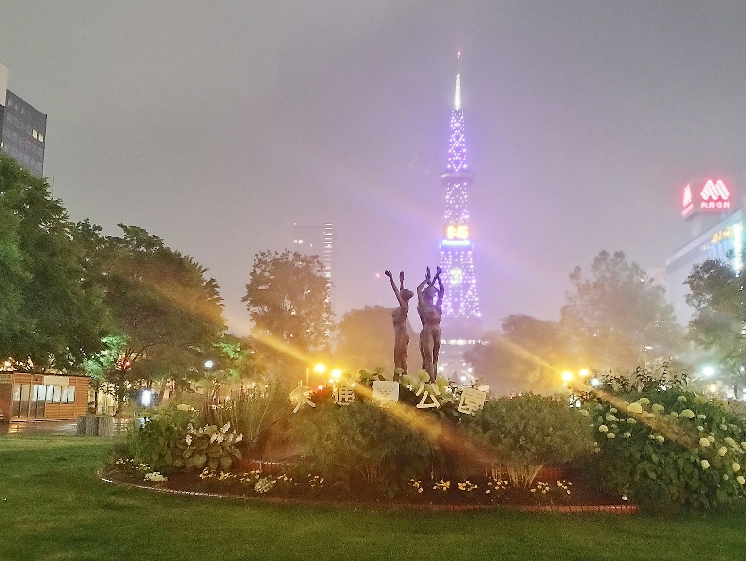 Parc de nuit avec deux statues en bronze et une tour illuminée en arrière-plan