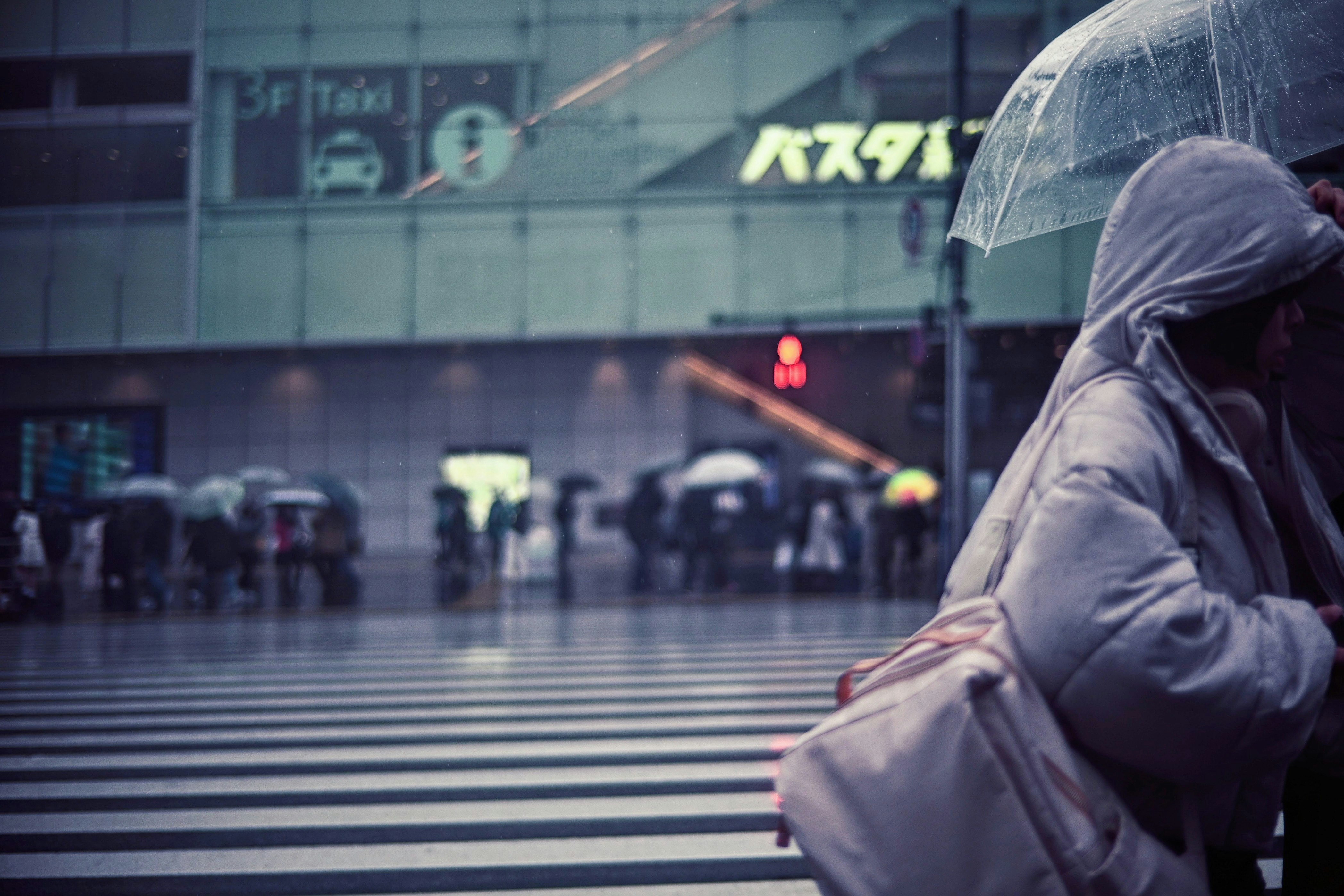 雨の駅前で傘をかぶる人々のストリート風景