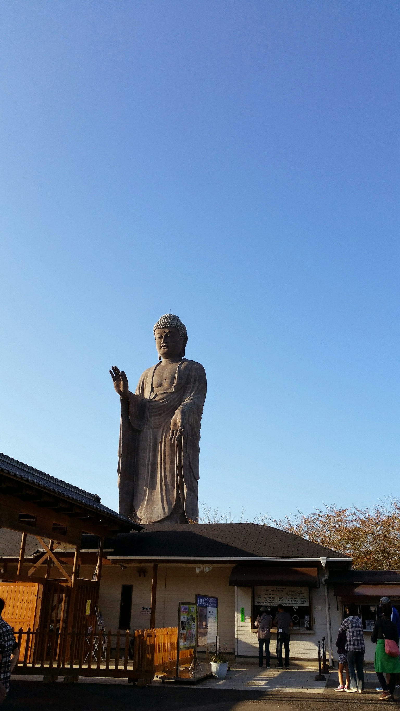 Patung Buddha besar di bawah langit biru cerah dengan orang-orang di dekatnya