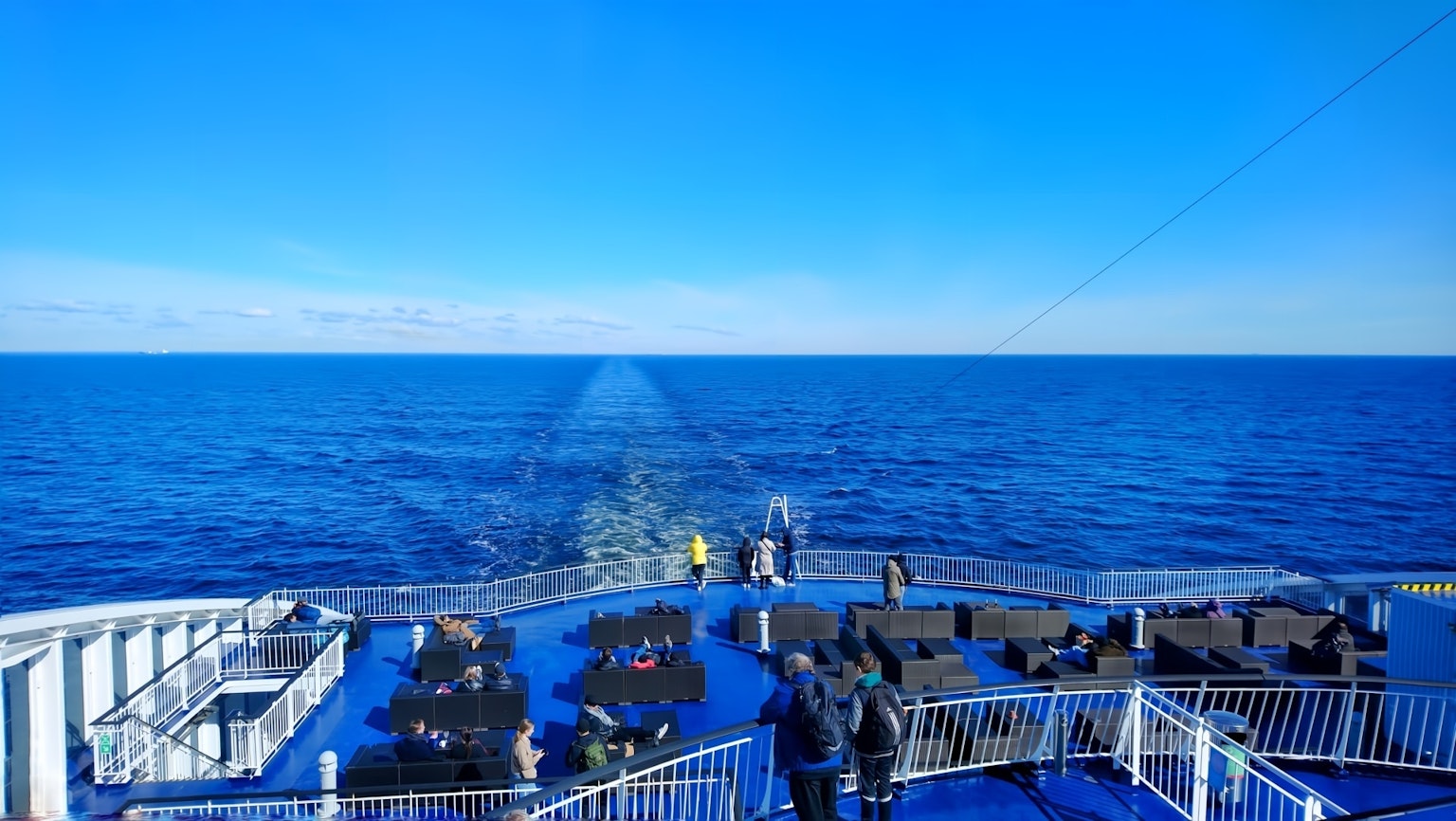 People on a ferry deck with a bright blue sea and sky