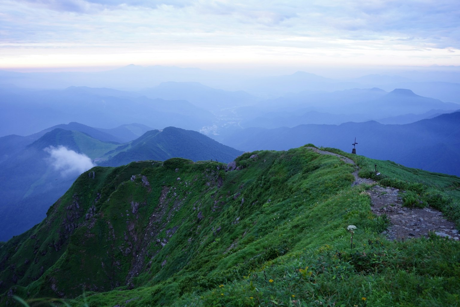 Cresta montañosa con hierba verde exuberante y montañas distantes bajo un cielo azul