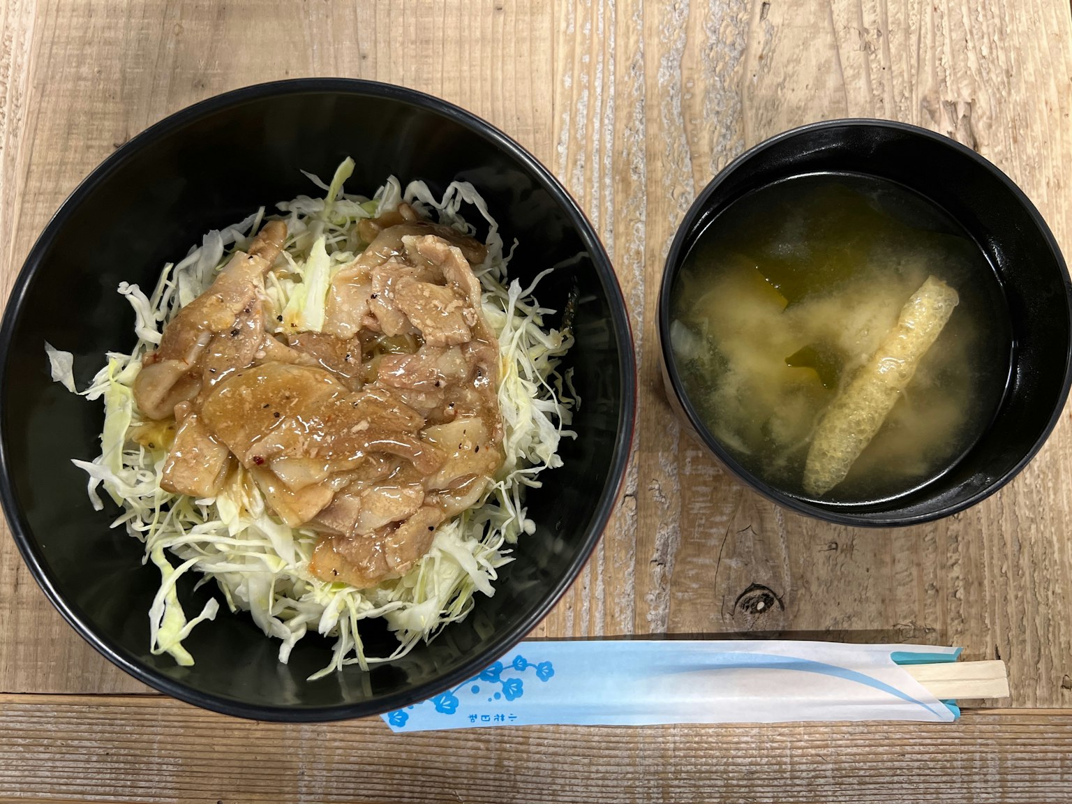 Un tazón negro con un plato de cerdo y repollo junto a una taza de sopa de miso