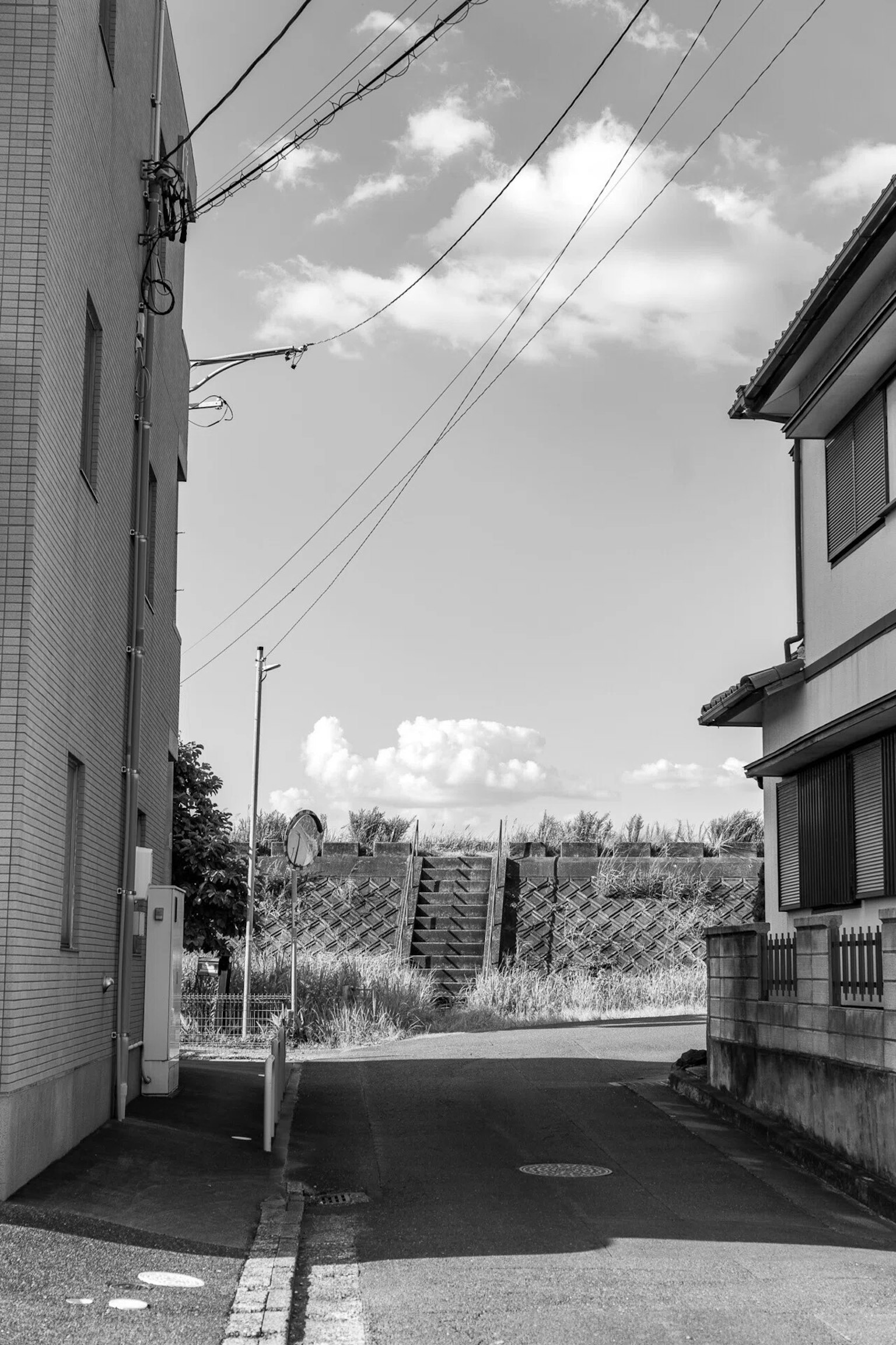 Städtische Szene in Schwarzweiß schmaler Durchgang zwischen zwei Gebäuden Wolken am Himmel sichtbare Stromleitungen