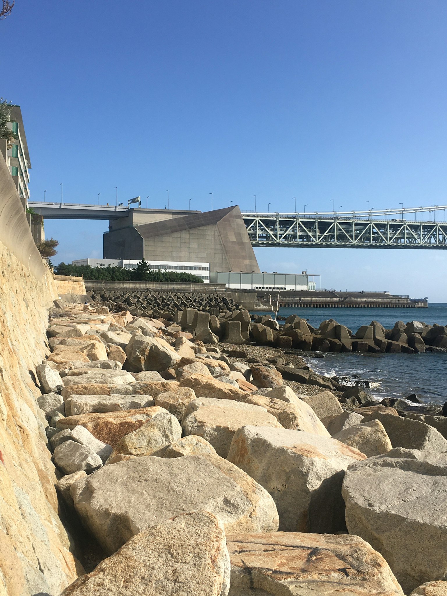 Coastal view featuring rocks and a modern building with a bridge
