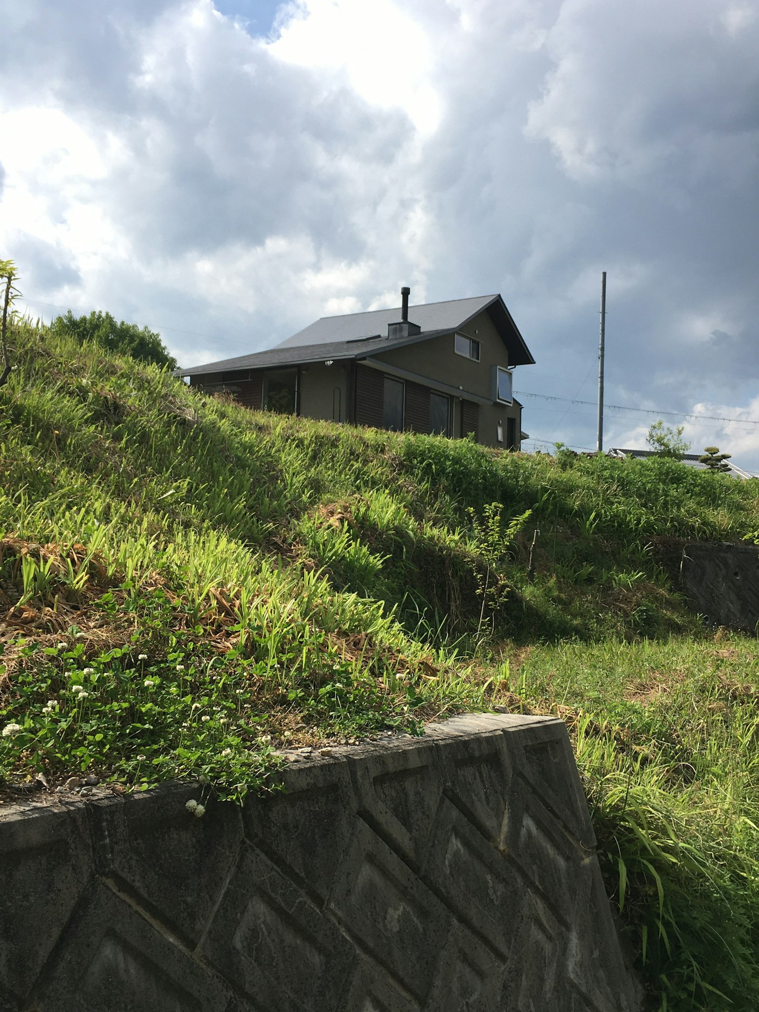 Sebuah rumah sederhana di atas bukit hijau dengan langit mendung