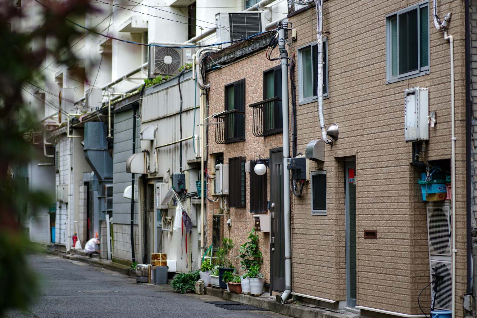 ด้านหน้าของอาคารที่อยู่อาศัยตามถนนแคบที่มีเครื่องปรับอากาศและพืชที่มองเห็นได้