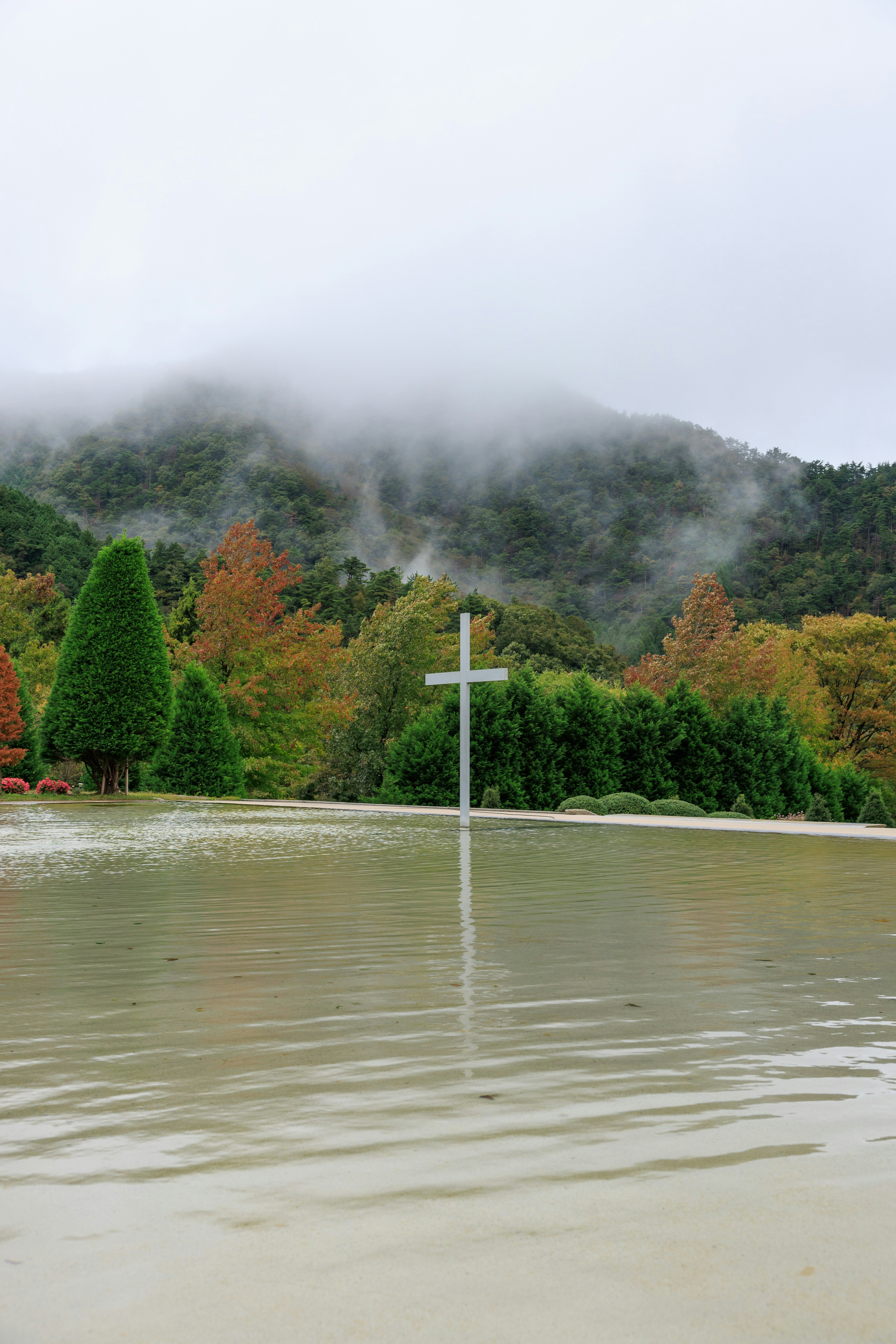 Kreuz am Ufer eines nebligen Sees mit Bäumen