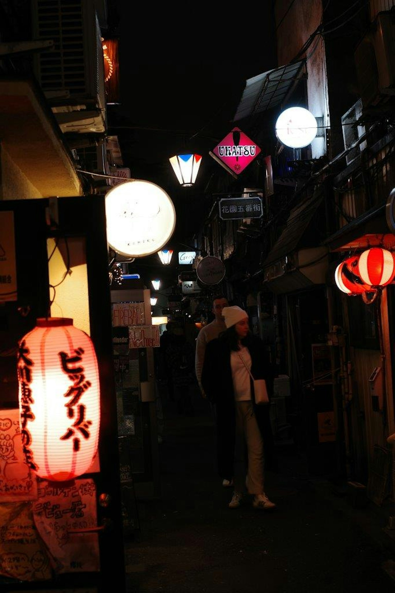 Schmale Gasse bei Nacht, beleuchtet von Laternen und Neonzeichen