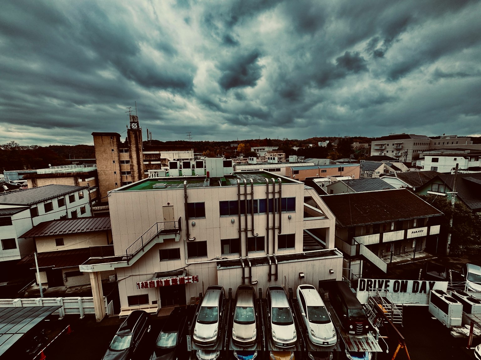 雲が広がる空の下にある都市の風景 駐車場に並ぶ車と建物が見える