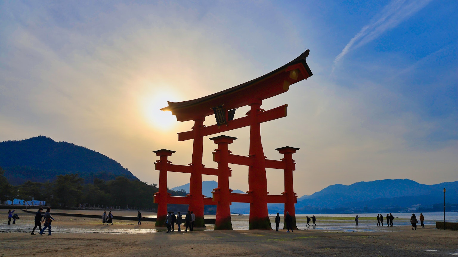 Silueta de una puerta torii roja con personas contra el atardecer
