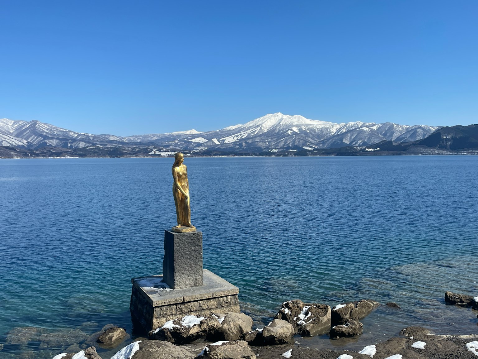 Estatua dorada cerca de un lago con montañas nevadas al fondo