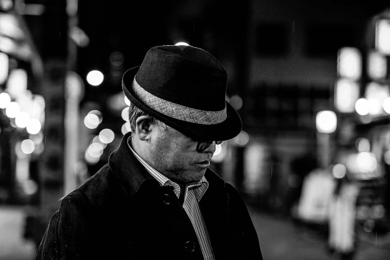 Un uomo con un cappello riflette nella città notturna