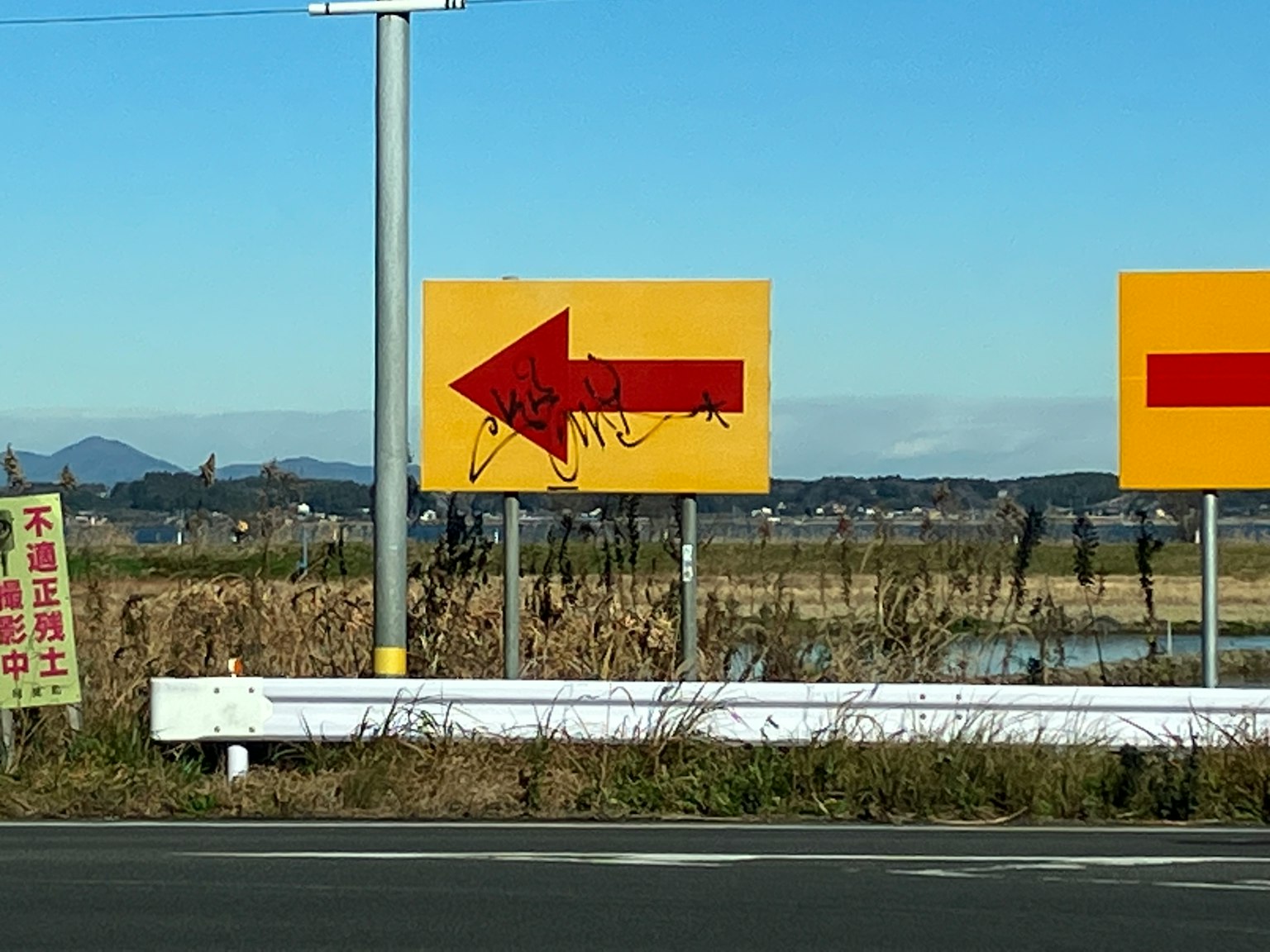 Señal direccional amarilla con flecha apuntando a la izquierda en un entorno rural