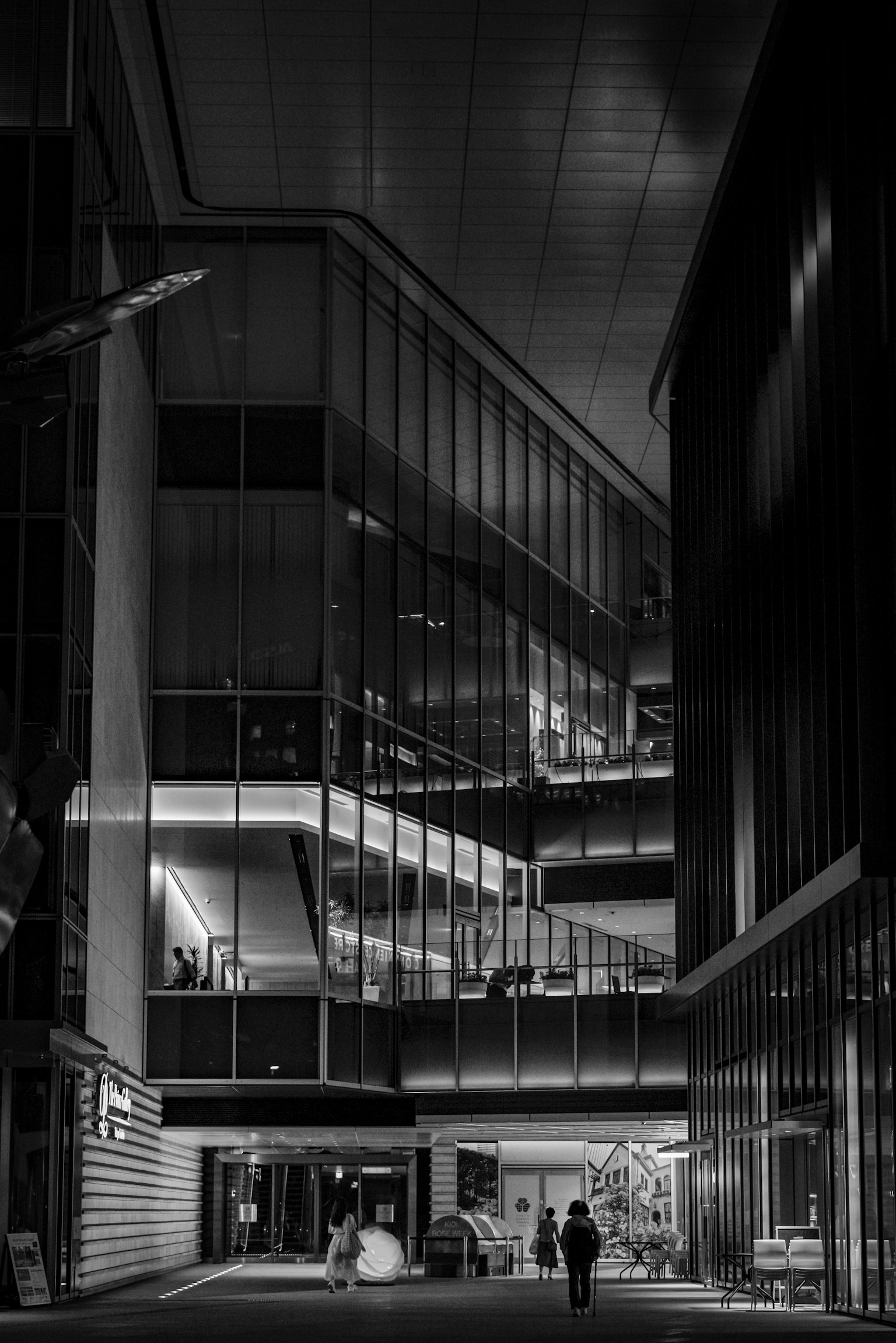 Silhouette di una persona che cammina tra edifici moderni di notte Facciate in vetro riflettente e illuminazione brillante